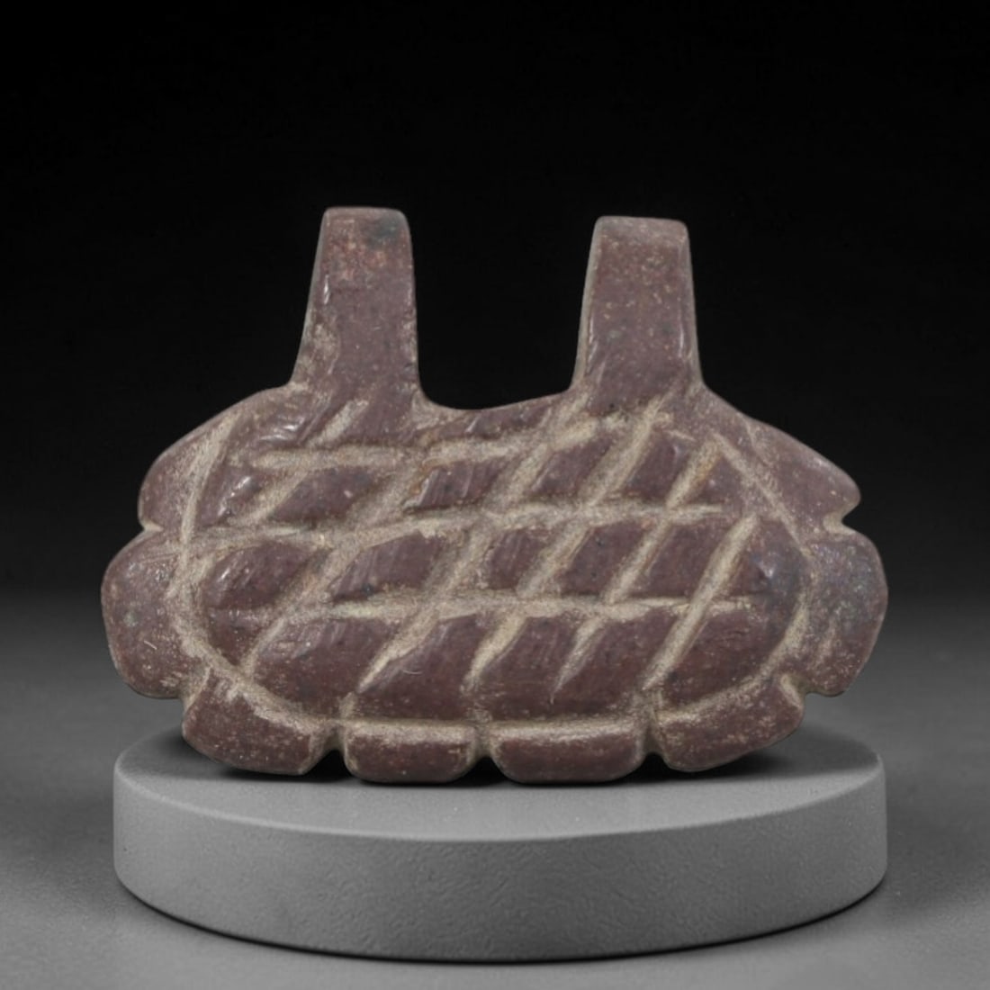 Ancient Stone Basket Amulet - Near Eastern Ritual Figurine, 91AR: Carved from a dense, dark stone with natural mineral inclusions and weathered patina, this amulet takes the form of a stylized basket with a scalloped lower edge and two vertical suspension loops at t