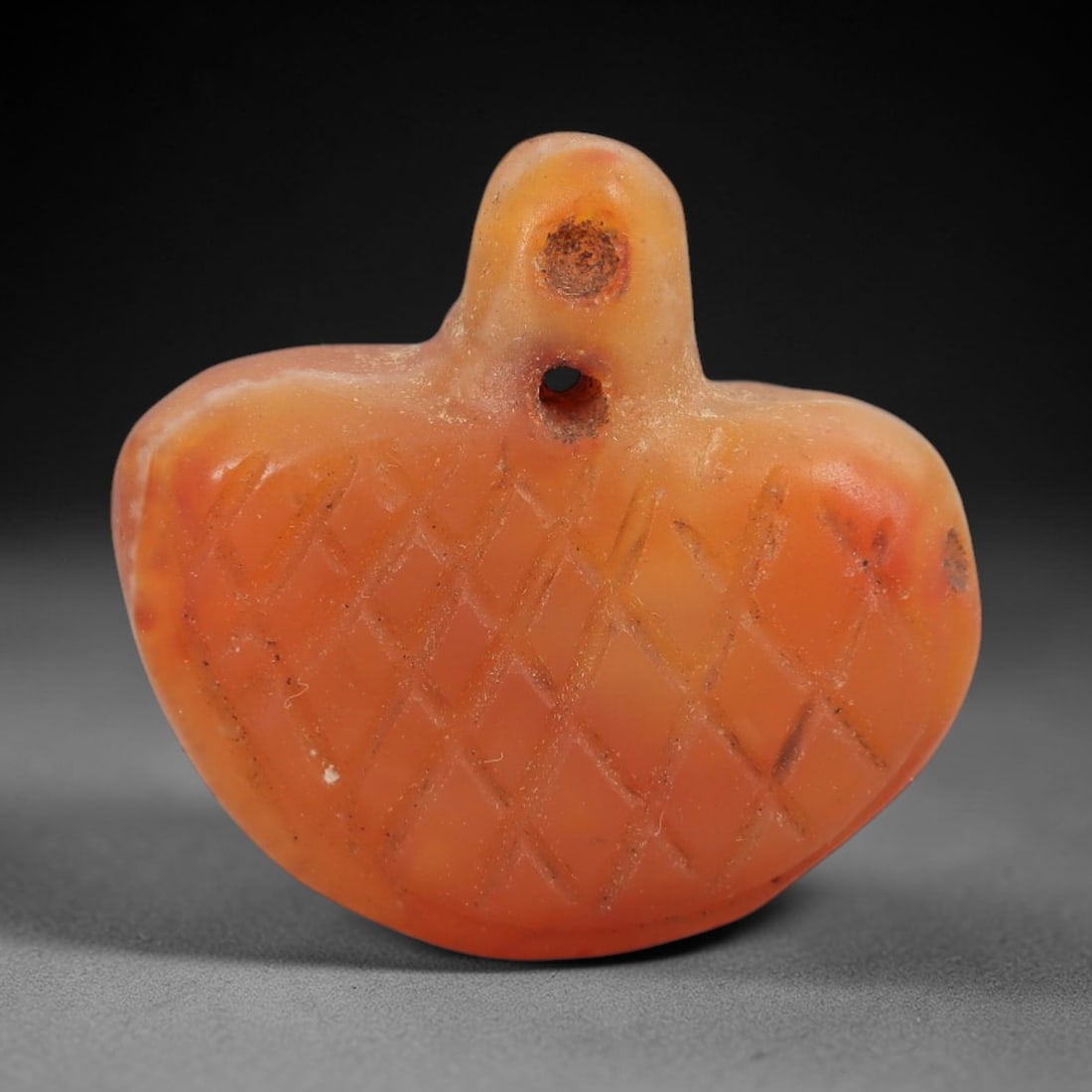 Ancient Carnelian Bird Amulet - Near Eastern Figurine, 30AJ: Carved from warm orange carnelian, this amulet is formed as a stylized bird with a rounded head and broad, heart-shaped body, featuring incised cross-hatching across the surface to denote feather or s