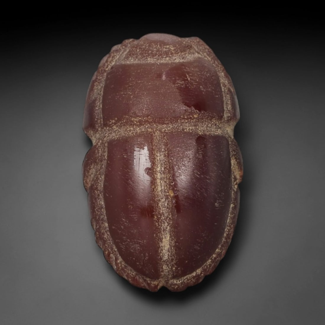 Ancient Red Jasper Scarab Amulet - Egyptian Figurine, 62AJ: Carved from deep, saturated red jasper, this amulet is formed as a stylized scarab beetle with incised linear detailing to define segmented body plates and distinct wing case contours, consistent with