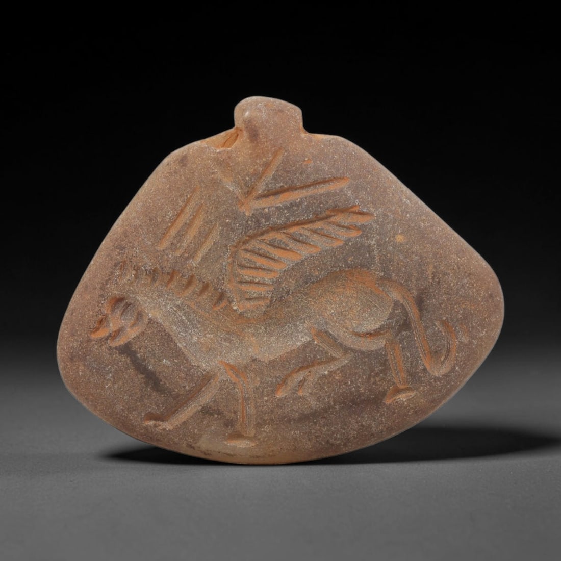 Ancient Stone Winged Horse Amulet - Near Eastern Pendant, 22WJ: Carved from stone, this ancient Near Eastern amulet pendant features a deeply incised relief of a winged horse (pegasus), rendered with linear carvings that define the creature's form, wings, and anat