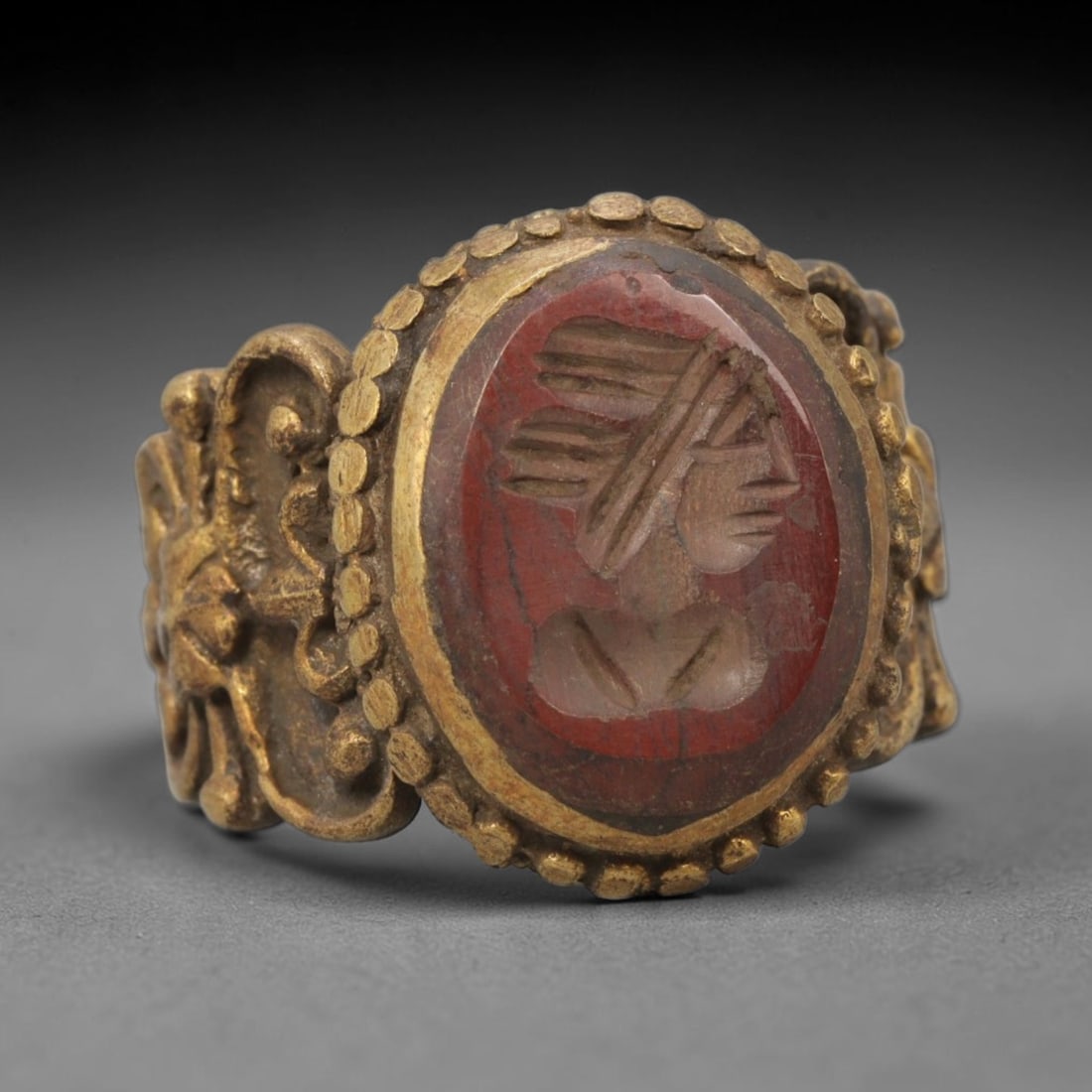 Antique Qajar Dynasty Carnelian Intaglio Ring - Size 10 US, 79ZX: Crafted from gilt brass with an ornate oval bezel, this ring features a carved carnelian intaglio stone at its center, depicting an incised profile portrait motif characteristic of Qajar-era Persian s