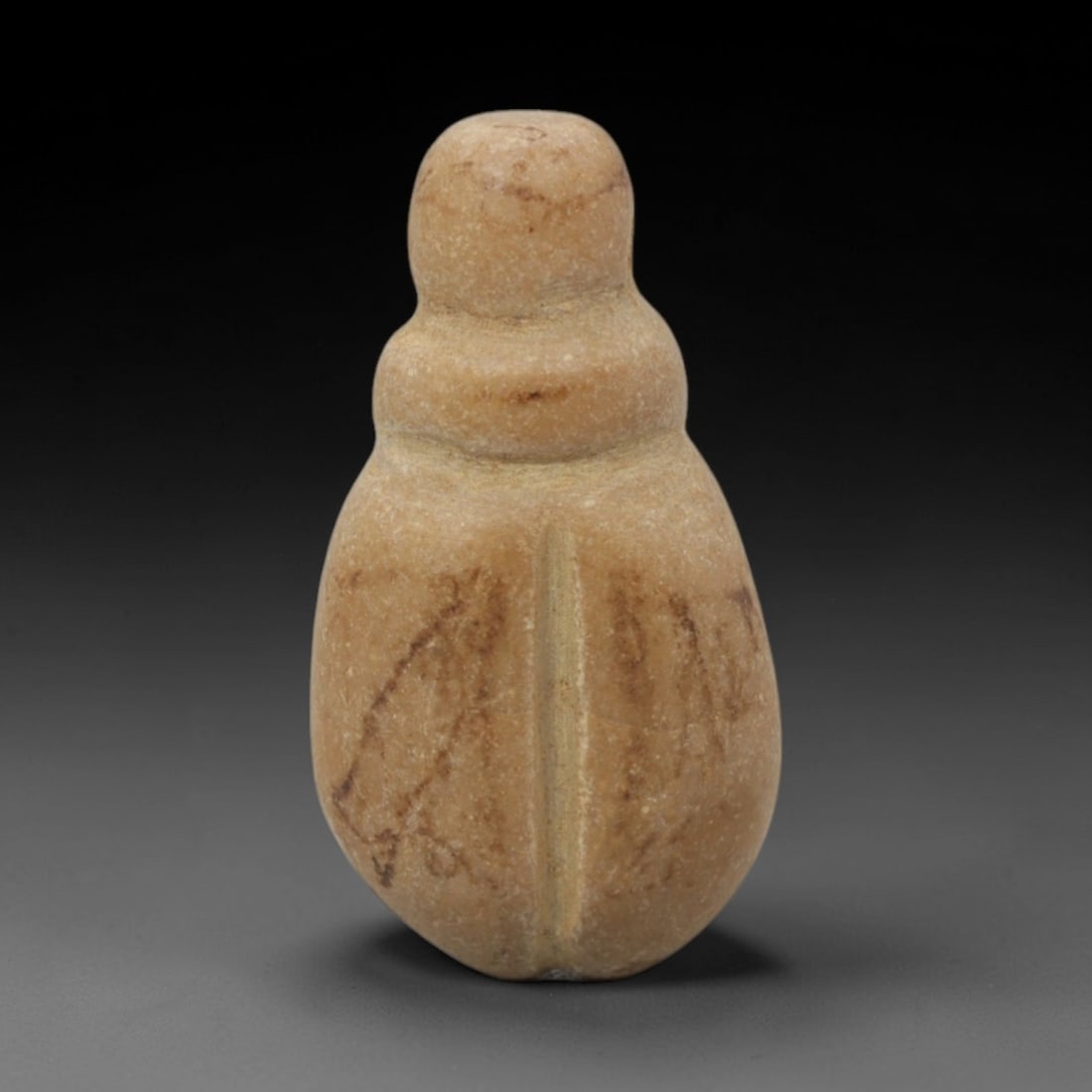 Ancient Stone Beetle - Egyptian Amulet Figurine, 24XR: Carved from pale beige stone with subtle reddish veining, this amulet depicts a stylized scarab beetle with a segmented body and a central vertical ridge representing the elytra. The form and iconogra