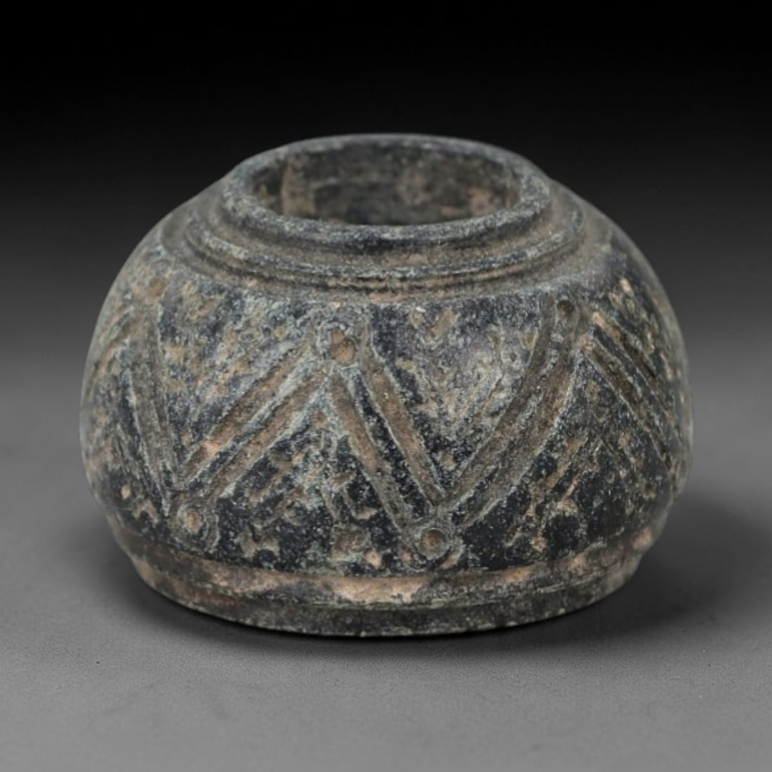 Ancient Bone Spindle Whorl - Near Eastern Triangular Motif, 78XR: This ancient Near Eastern spindle whorl is carved from bone, featuring a convex form with a central perforation. The surface is incised with triangular and linear motifs, a common decorative technique