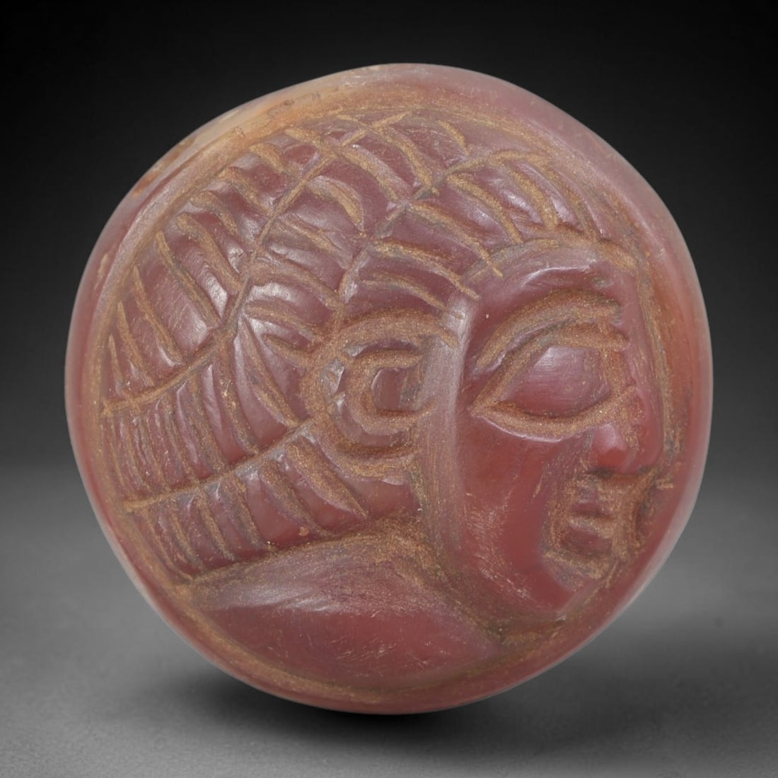 Ancient Carnelian Head Plaque - Near Eastern Amulet, 46FY: Carved from a rich reddish-brown carnelian agate, this amulet takes the form of a stylized human head in high relief, set within a circular plaque, characteristic of ancient Near Eastern amuletic and