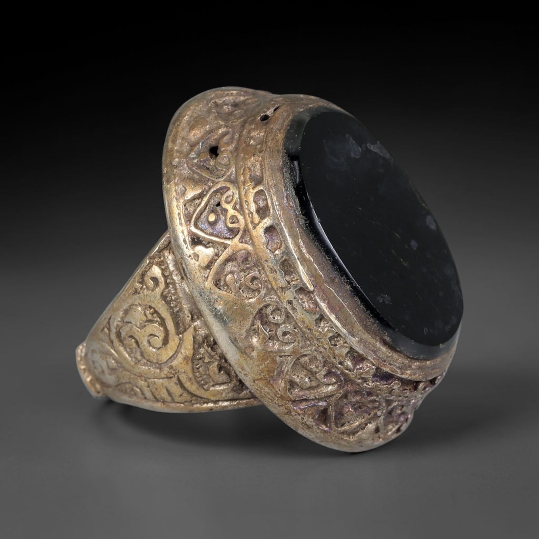 Antique Qajar Dynasty Silvered Black Stone Signet Ring - US Size 8, 66BA: This antique ring, crafted during the Qajar Dynasty of Persia, features a large oval black stone set in a domed, silvered bezel. The bezel and ring shoulders are adorned with intricate engraved Islami