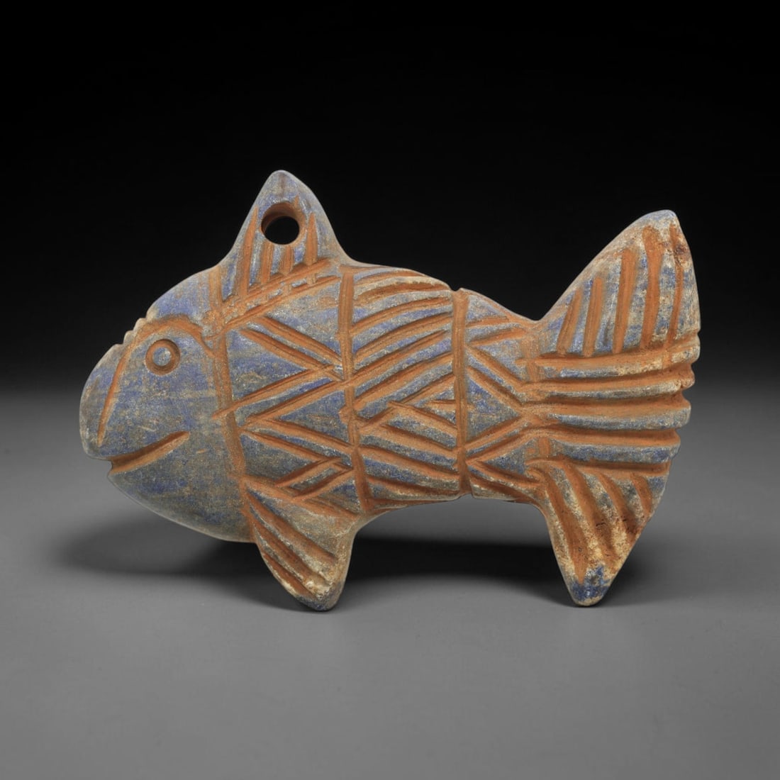 Ancient Lapis Fish Amulet - Near Eastern Carved Figurine, 73ZT: Carved from lapis lazuli, the amulet takes the form of a stylized fish, rendered in flat relief with incised geometric and linear decoration. A suspension hole is drilled through the dorsal fin for we