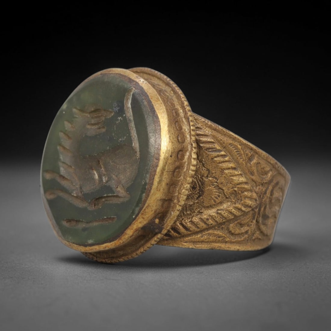 Antique Qajar Dynasty Green Intaglio Ring - Size 7 US, 1WJ: Crafted from gilt brass with a rounded bezel, this ring features a carved green stone intaglio at its center, incised with a stylized quadruped motif characteristic of Qajar-era Persian symbolic carvi
