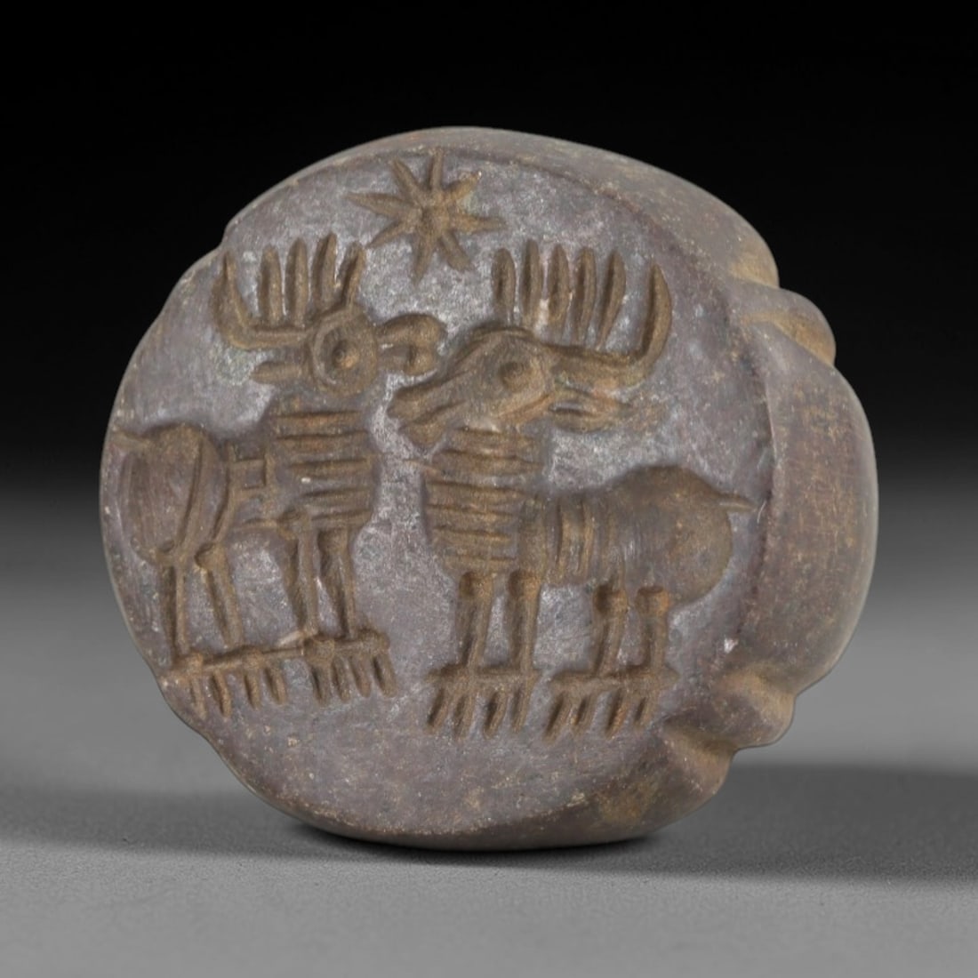 Ancient Steatite Stamp Seal - Sasanian Two Stags, 63AK: Carved from steatite, this hemispherical Sasanian stamp seal features a central composition of two stylized stags beneath a star motif, with simplified linear detailing defining their antlers, bodies,