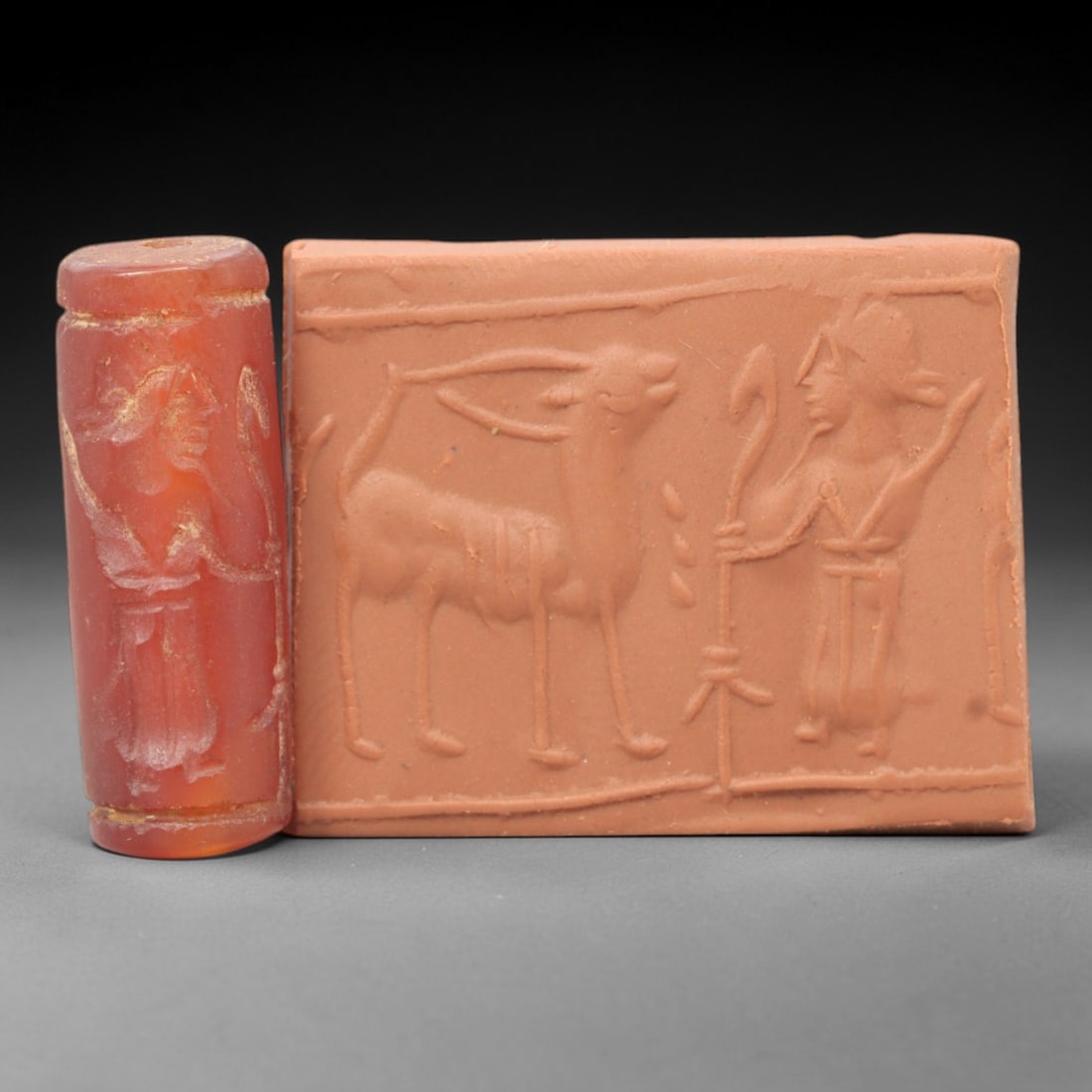 Ancient Carnelian Cylinder Seal - Mesopotamian Ibex & Winged Figure Scene, 71ZS: Carved from rich red carnelian, this ancient Mesopotamian cylinder seal features a refined linear relief composition of a standing ibex and a winged humanoid figure holding staffs, executed in the cha