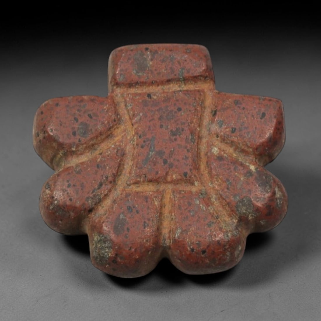 Ancient Red Stone Cross Amulet - Near Eastern Geometric Pendant, 70XP: Carved from a speckled, deep red stone, this miniature amulet features a symmetrical cross-shaped form with rounded, lobed terminals, a distinctive geometric motif in ancient Near Eastern ritual art.