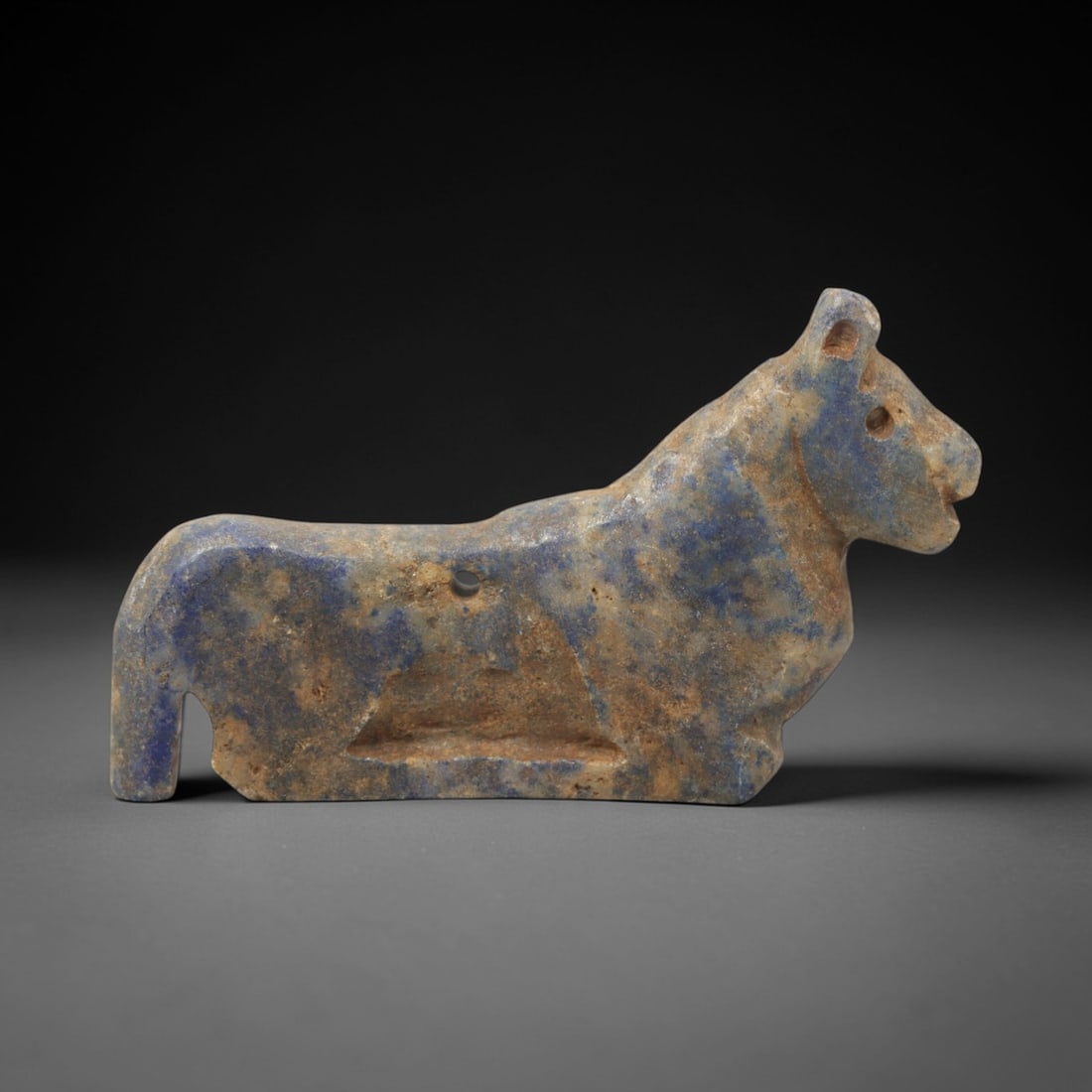 Ancient Lapis Lazuli Feline - Near Eastern Amulet Figurine, 44XV: Carved from lapis lazuli, this feline amulet is rendered in a stylized recumbent pose, with simplified anatomical details and a drilled suspension hole consistent with wearable amuletic function. The