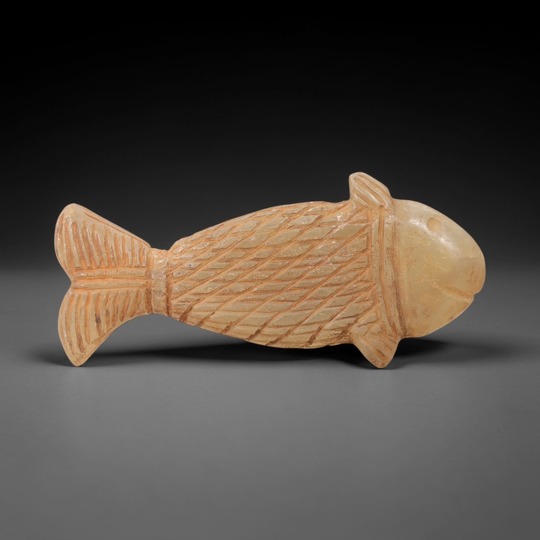 Ancient Chalcedony Fish - Near Eastern Amulet Figurine, 4AL: Carved from translucent chalcedony, this amulet depicts a stylized fish form with incised linear details defining the scales, fins, tail, and facial features, including a defined eye and mouth. Attrib