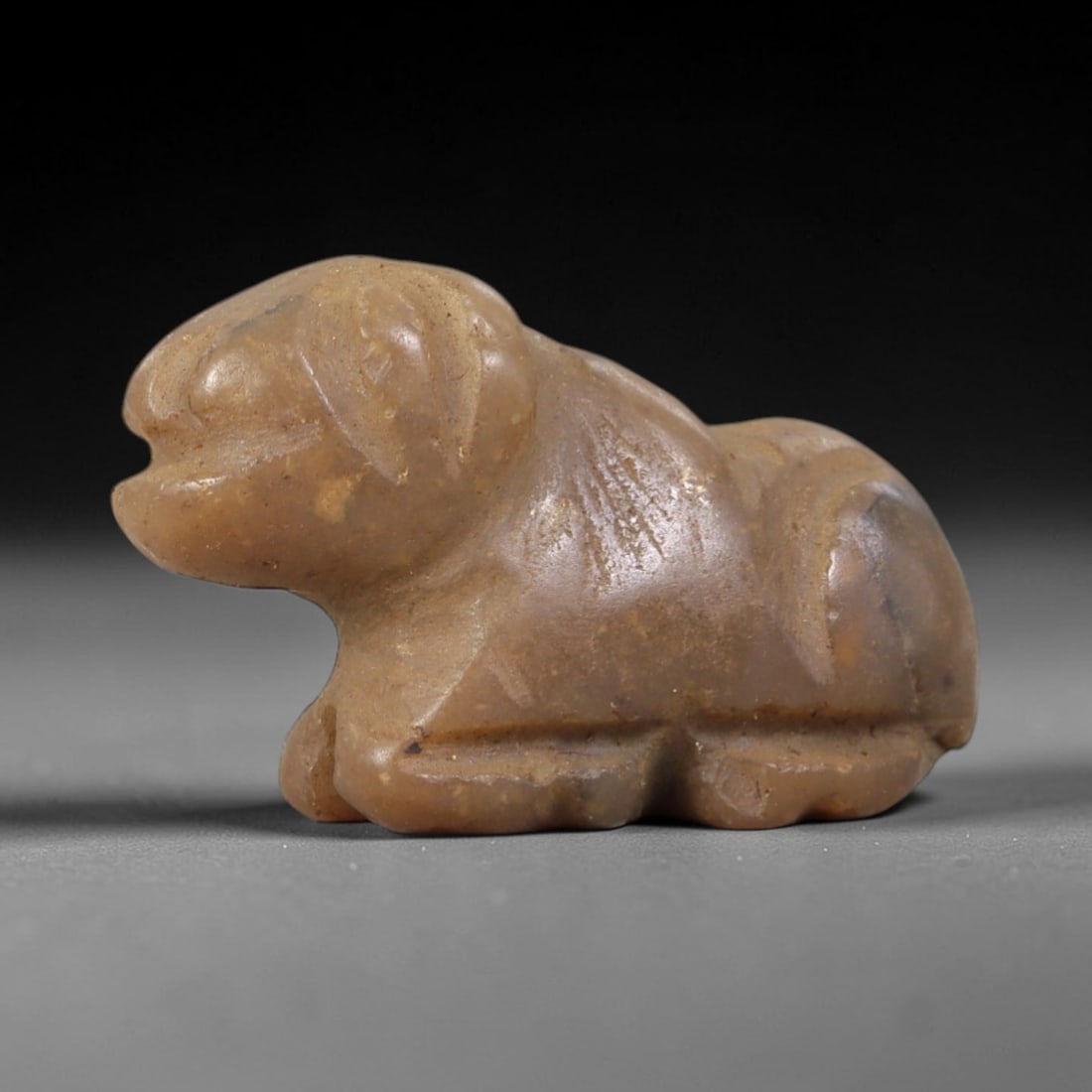 Ancient Stone Zoomorphic Feline - Near Eastern Amulet Figurine, 41AS: Carved from mottled hardstone, this amulet depicts a recumbent zoomorphic feline form with stylized, geometric features. The head is rounded with incised eye motifs and a broad snout, while the body i