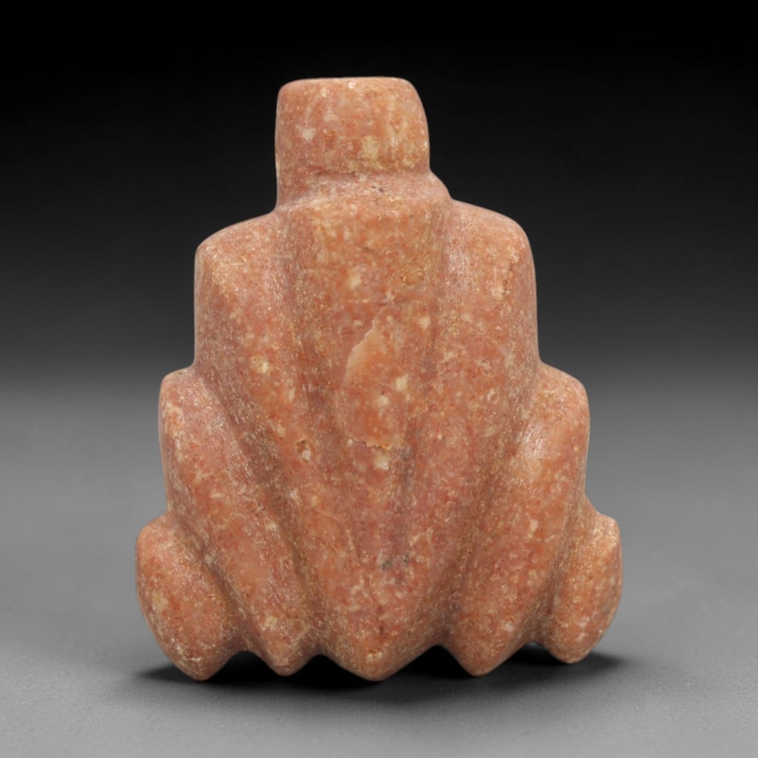 Ancient Red Stone Frog Amulet - Egyptian Animal Figure, 43ZW: This amulet is carved from speckled warm red stone, depicting a stylized frog in a crouched posture with simplified, rounded limbs and a broad, tapering body. A cylindrical suspension knob is present