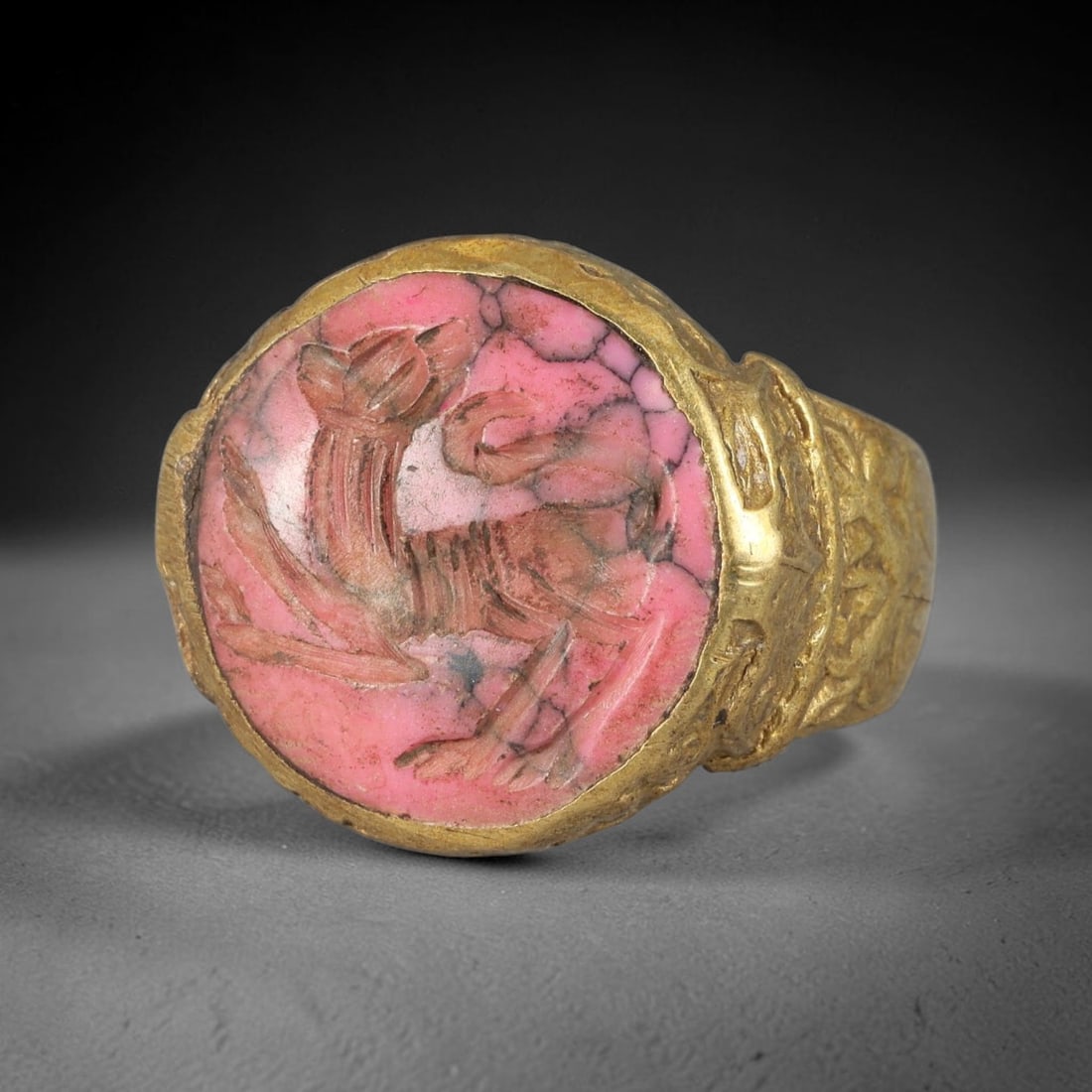 Antique Qajar Dynasty Rhodonite Ibex Intaglio Ring - Size 7 US, 95FY: Crafted from gilt brass with an ornate circular bezel, this ring features a carved rhodonite intaglio stone at its center, incised with a detailed stylized ibex (wild goat) motif-an ancient amuletic s