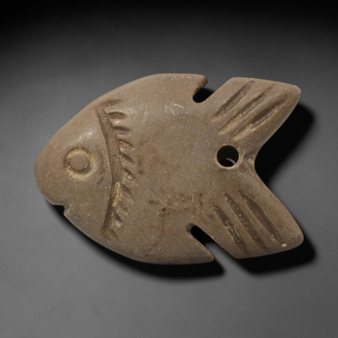 Ancient Stone Fish - Egyptian Amulet Pendant, 82XQ: Carved from light brown stone, this amulet depicts a stylized fish with incised linear details defining its fins, tail, and facial features, including a drilled suspension hole for threading as a wear