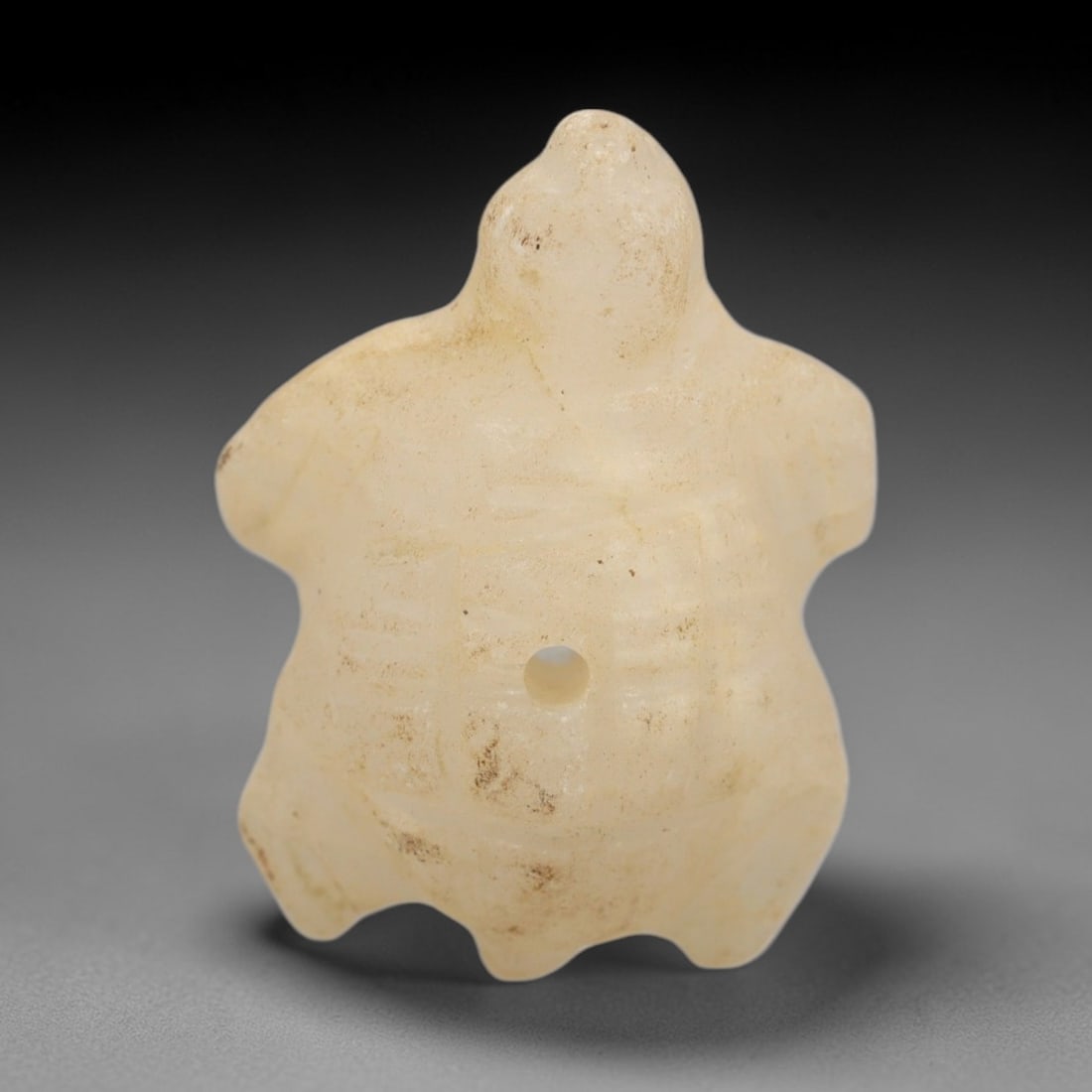 Ancient Calcite Turtle Amulet - Egyptian Animal Figure, 28ZW: This amulet is carved from translucent pale calcite, depicting a stylized turtle with a rounded carapace, simplified limbs, and a small raised head. Incised lines texture the shell to mimic natural se