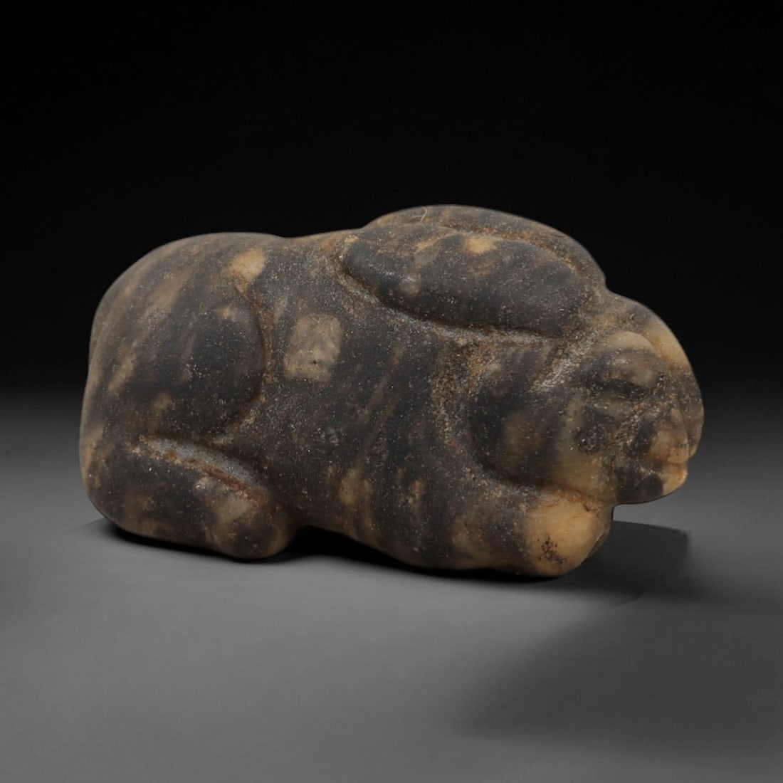Ancient Mottled Stone Hare Amulet - Near Eastern Relic, 83AD: Carved from dark brown and beige mottled stone, this amulet depicts a stylized hare in a compact, recumbent form. The creature features simplified facial contours, rounded ears, and a robust body, ref