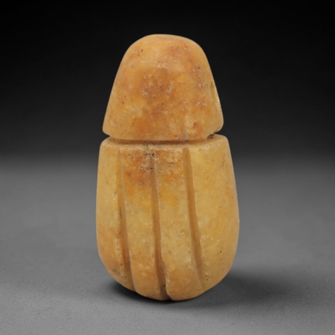 Ancient Egyptian Fly Amulet - Egyptian Stone Pendant, 38XQ: This amulet is carved from a pale, yellowish-tan stone, shaped into a stylized fly form with a rounded head and segmented body, featuring incised vertical grooves that define the insect's wing segment