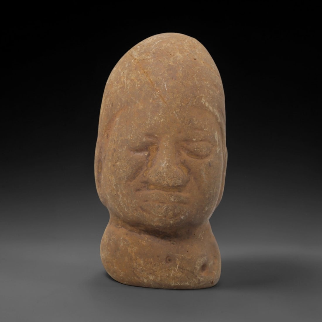 Ancient Stone Bust - Near Eastern Anthropomorphic Figurine, 82FW: Carved from a fine-grained, earthy stone, this Near Eastern bust presents a stylized human head with a rounded, domed upper form, recessed eye sockets, a defined nasal ridge, and a closed mouth. The c