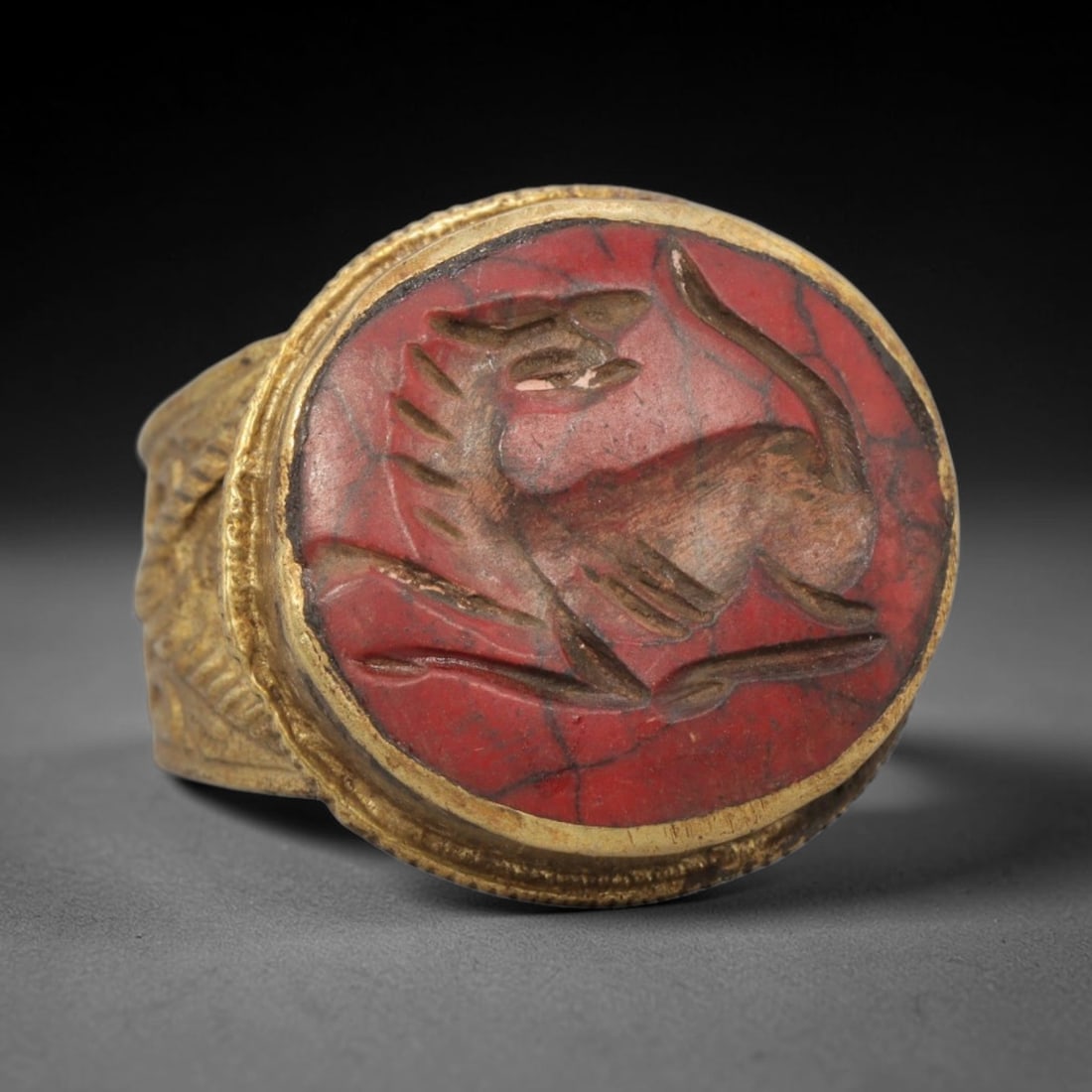Antique Qajar Dynasty Red Stone Intaglio Ring - Size 7 US, 97ZX: Crafted from gilt brass with a rounded bezel, this ring features a carved red stone intaglio at its center, incised with a stylized feline or canine quadruped motif characteristic of Qajar-era Persian