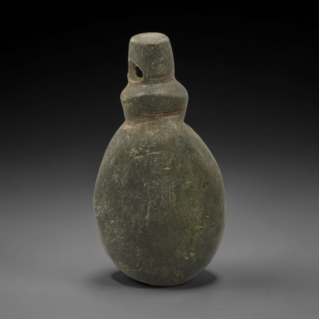 Ancient Stone Pendant - Near Eastern Amulet, 43XR: Carved from dark green stone, this amulet features a teardrop-shaped body with a cylindrical top section pierced for suspension, consistent with Ancient Near Eastern pendant craftsmanship of the Iron