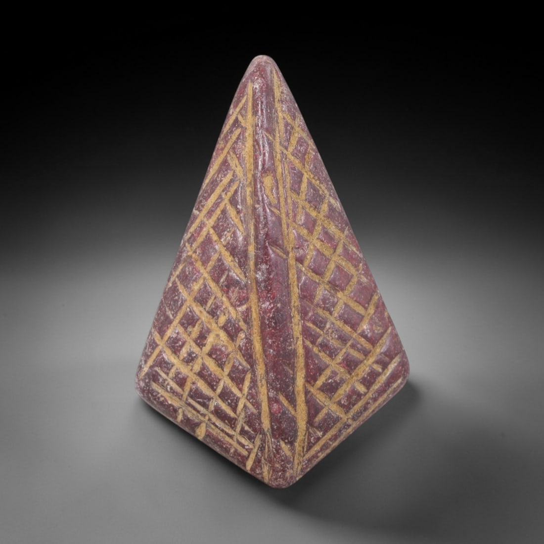 Ancient Stone Pyramidion Amulet - Egyptian Geometric Figurine, 82AP: Carved from a dense, reddish-brown stone with lighter mineral inclusions, this amulet takes the form of a tapering pyramidion, the apex of an Egyptian pyramid. Its surfaces are decorated with incised