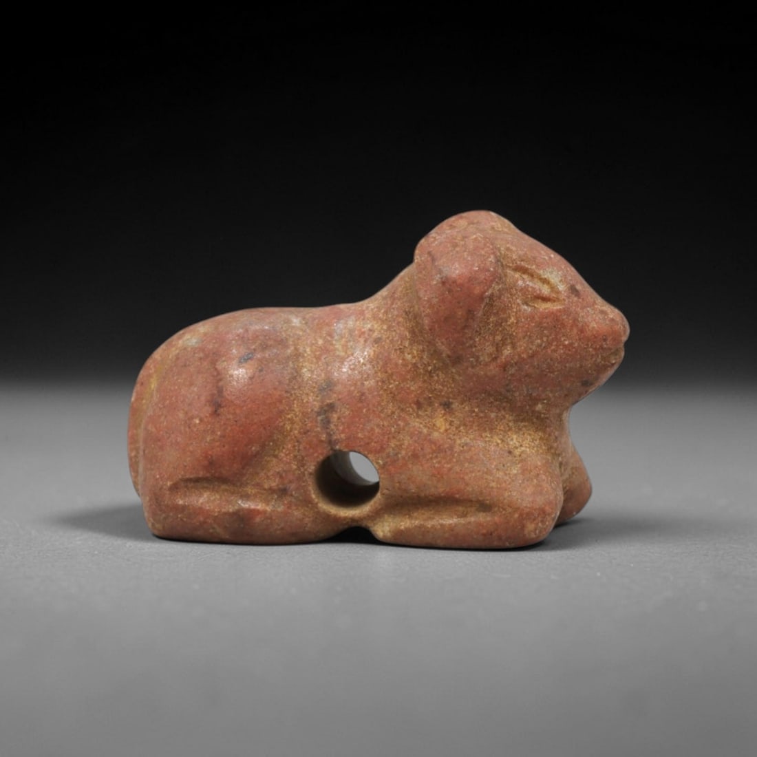 Ancient Stone Bovine Amulet - Near Eastern Figurine, 6XT: This amulet is carved from a warm reddish stone with natural earthy patina and subtle tonal variations across its surface, executed in a simplified, stylized manner that emphasizes the recumbent bovin