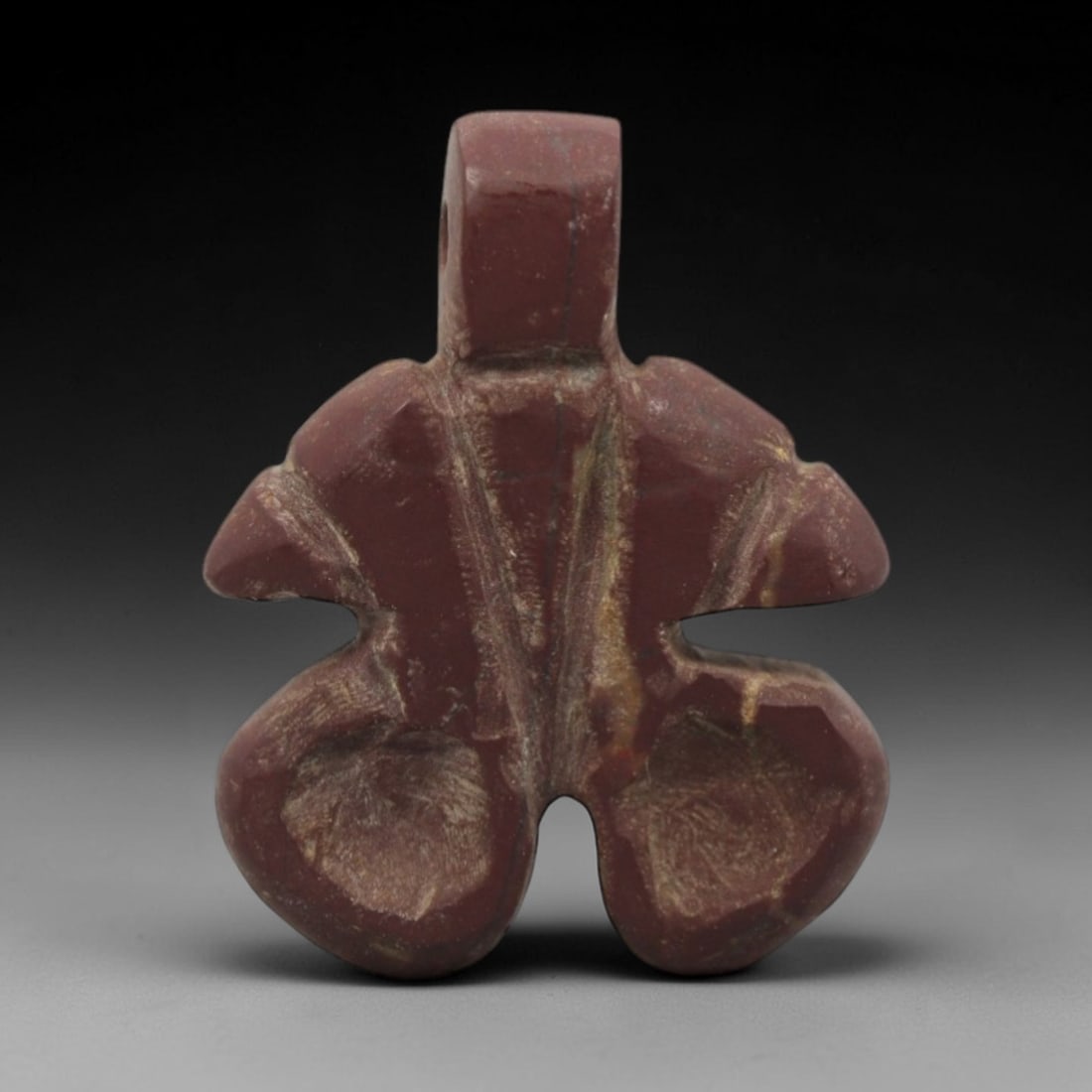 Ancient Near Eastern Stone Double Amulet - Carved Pendant Figure, 99ZW: This amulet is carved from a rich, reddish-brown stone with natural veining, likely a type of siltstone or jasper, with incised linear details defining its symmetrical double form. The piece features