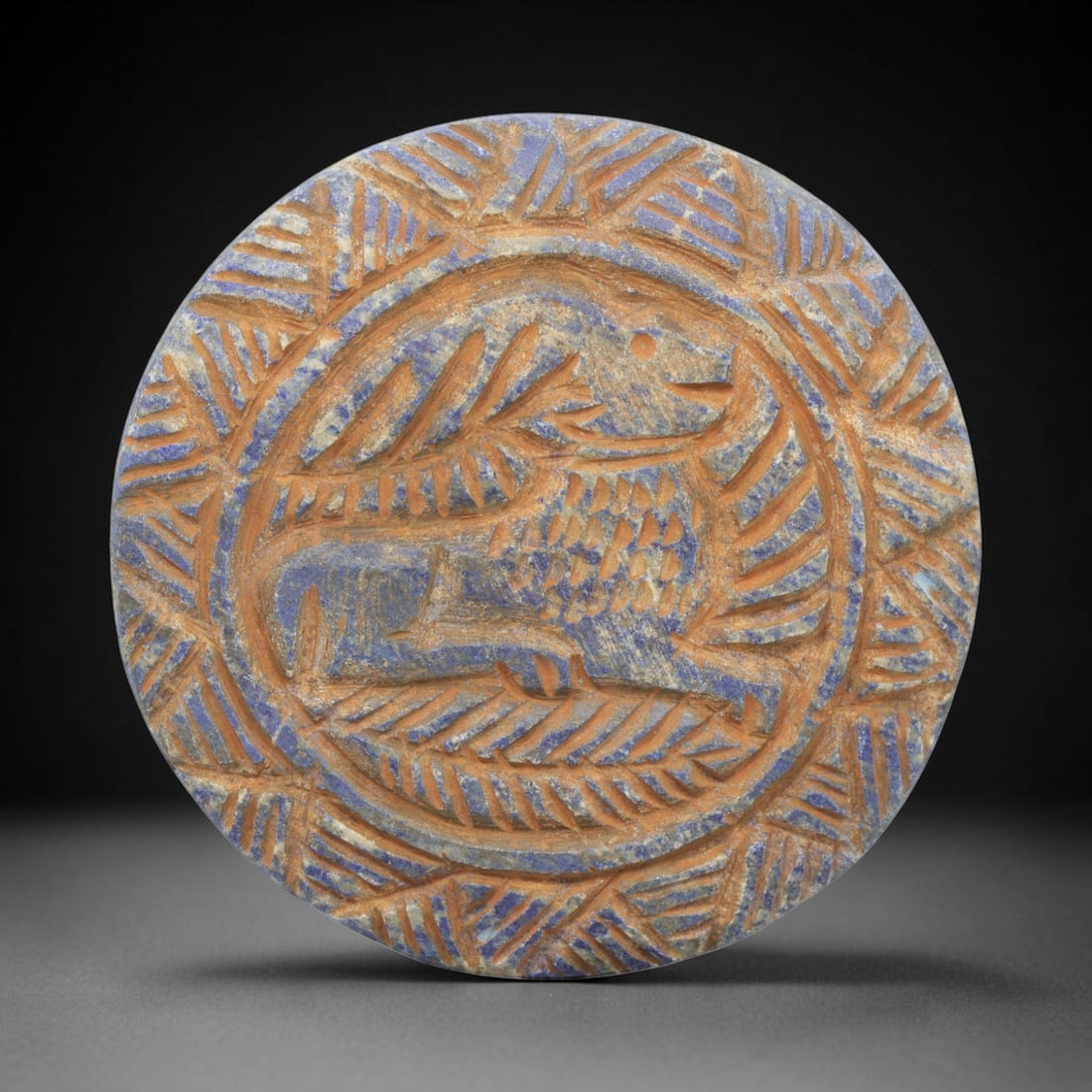 Ancient Lapis Lazuli Ibex Amulet - Near Eastern Carved Disk, 18WJ: Carved from lapis lazuli, this circular disk features a deeply incised central motif of a standing ibex, rendered in profile with a curved horn, stylized body, and incised details to denote fur and mu