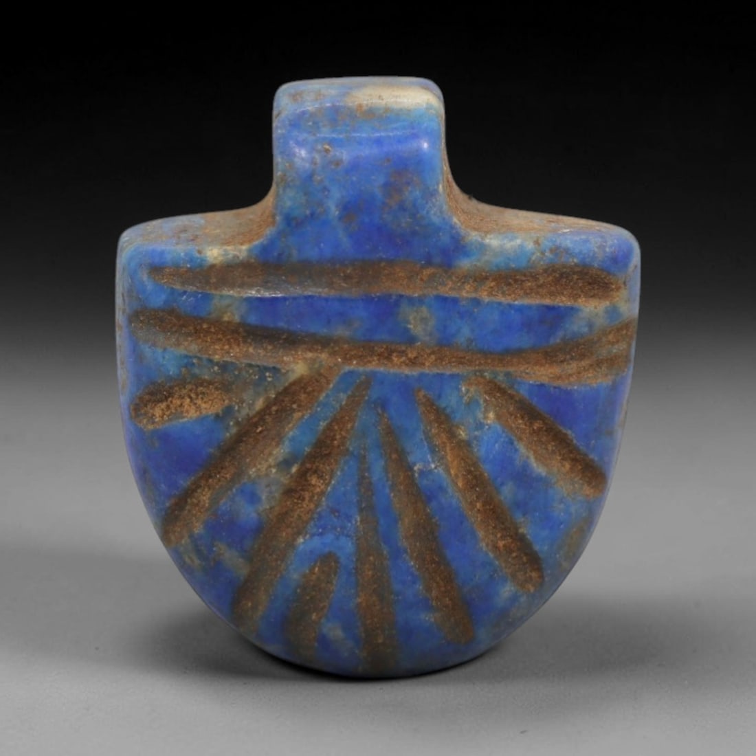 Ancient Lapis Lazuli Amulet - Egyptian Ritual Pendant, 27ZT: Carved from lapis lazuli, this amulet features a shield-shaped form with a raised rectangular upper lug pierced for suspension, its surface incised with radiating linear details that define symbolic p
