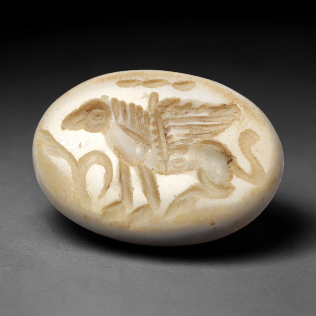 Ancient Agate Intaglio Bead - Near Eastern Griffin Motif, 37ZW: Carved from pale banded agate, this oval intaglio bead features a recessed depiction of a winged griffin, with incised linear detailing to denote feathered wings, quadrupedal anatomy, and a curled tai