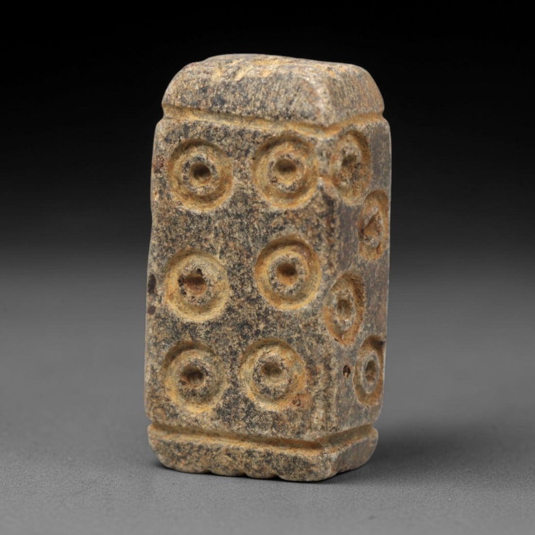 Ancient Steatite Amulet Bead - Near Eastern Concentric Circles, 16XV: Carved from dense steatite, this ancient amulet bead takes a rectangular prism form, with a vertical suspension hole for wearable use. Its visible faces are decorated with multiple raised concentric c