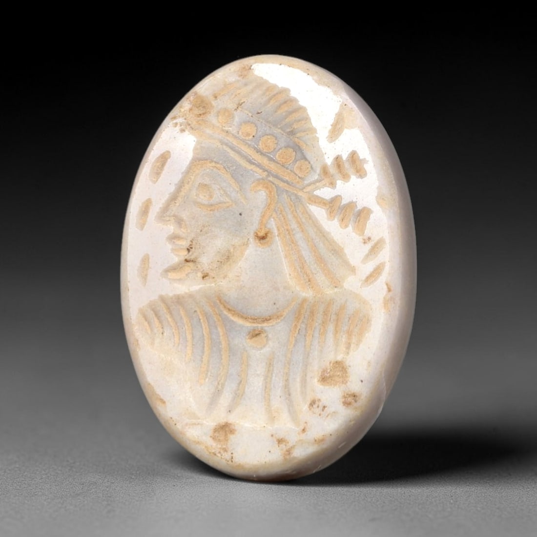 Ancient Stone Royal Bust Intaglio - Near Eastern Amulet, 100AP: This oval intaglio is carved from a pale, creamy stone matrix, featuring a high-relief profile depiction of a royal or divine figure, adorned with an elaborate beaded headdress and incised linear deta