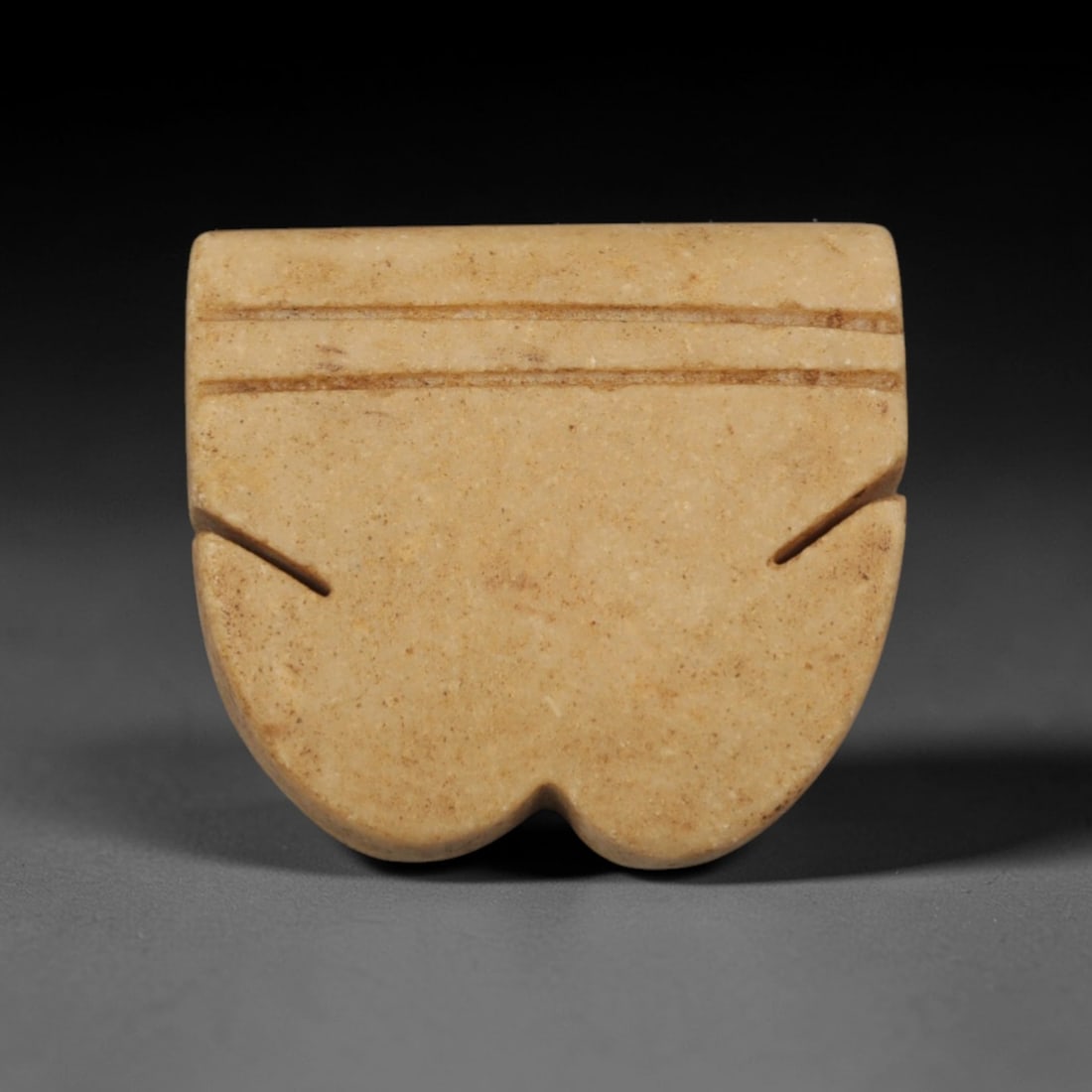 Ancient Cream Stone Heart-Form Pendant - Near Eastern Ritual Amulet, 100XP: Carved from a smooth, creamy-tan stone, this miniature pendant features a stylized heart-shaped lower half with a rectangular upper section, a distinctive geometric motif in ancient Near Eastern ritua