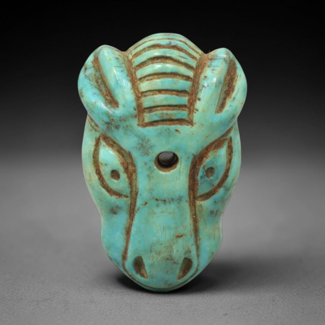 Ancient Turquoise Amulet - Near Eastern Horse Head Figurine, 10XV: Carved from vibrant turquoise, this amulet is skillfully rendered in the form of a horse head, featuring incised linear striations detailing the mane, stylized almond-shaped eyes, and defined nostrils