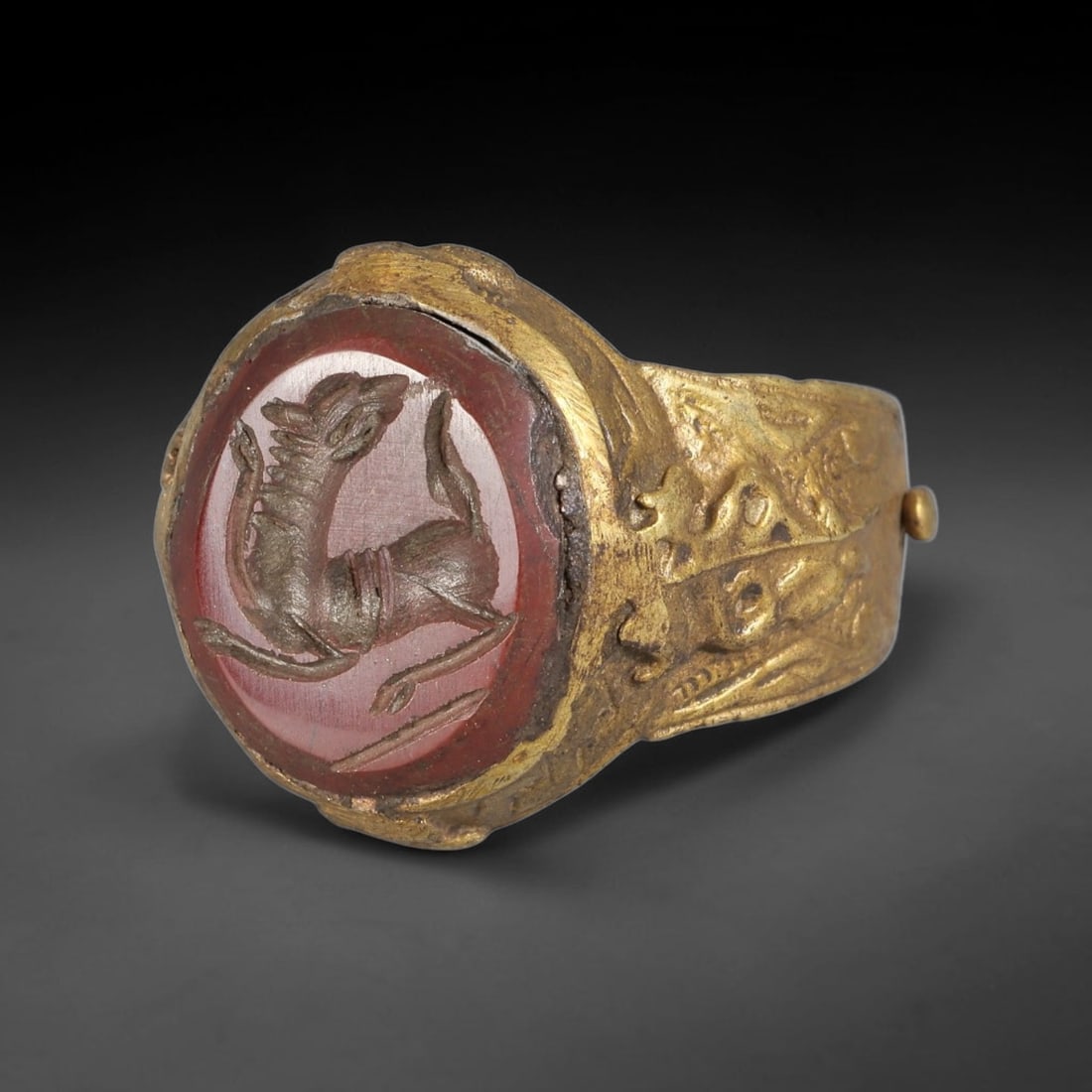 Antique Qajar Dynasty Carnelian Intaglio Brass Ring - Size 10 US, 74BA: Crafted from brass, this ring features a circular carnelian intaglio panel carved with a stylized quadruped in a dynamic pose, executed in the traditional Qajar style. The brass band displays ornate,