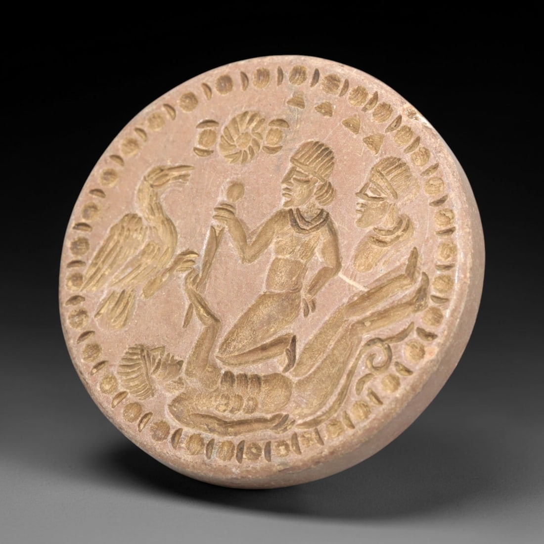 Antique Stone Intaglio - Near Eastern Style Figural Seal, 61ZP: This circular intaglio is carved from warm-toned stone, featuring a narrative relief scene with two seated figures, a reclining figure, and a large bird of prey, surrounded by geometric and floral bor