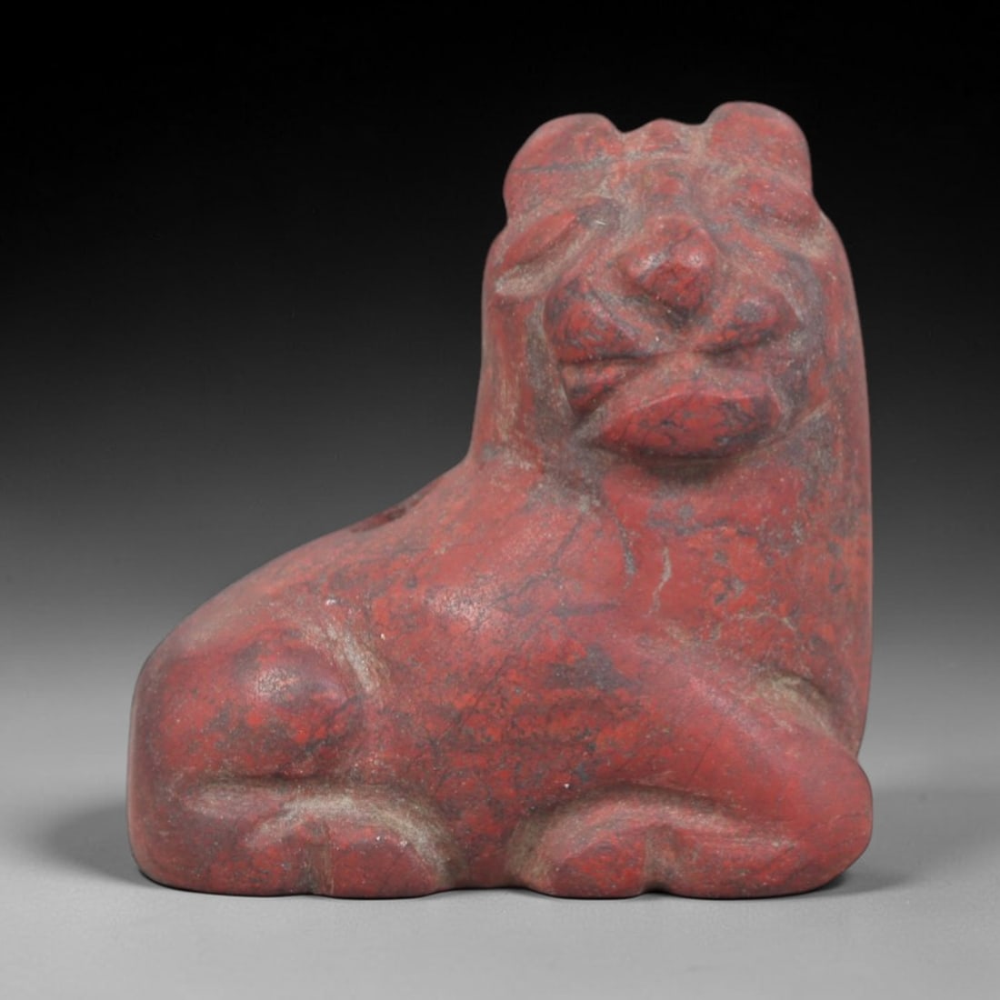 Ancient Stone Lion - Egyptian Amulet Figurine, 30AP: This artifact is carved from variegated red stone with a weathered patina and subtle mineral veining, exhibiting stylized facial detailing and a compact seated form consistent with ancient Egyptian st