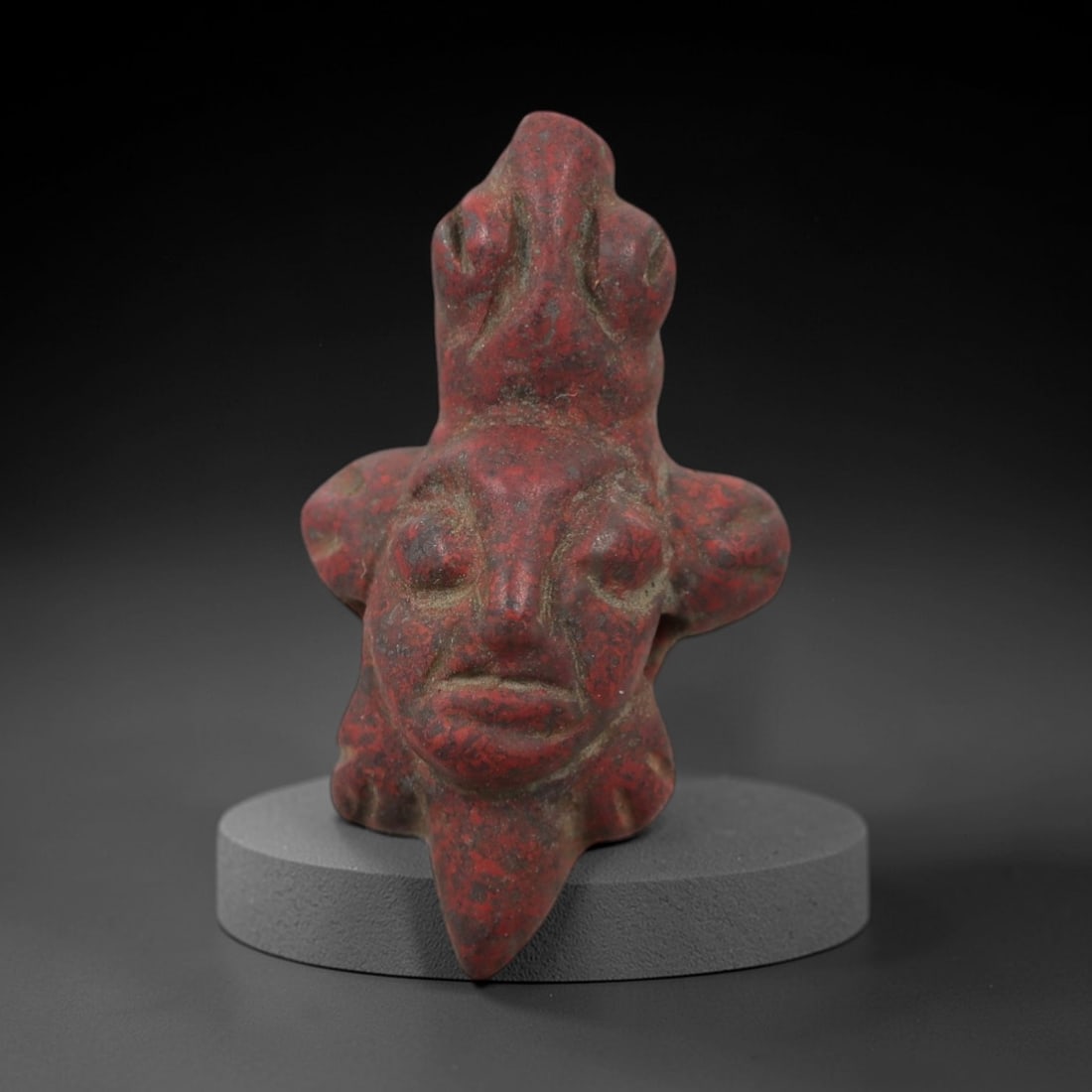 Ancient Stone Anthropomorphic Head Amulet - Near Eastern Ritual Figurine, 6AG: This amulet is carved from a single piece of mottled red stone, exhibiting a granular texture with earthy grey patina and subtle mineral inclusions across its surface. The form is stylized as an anthr