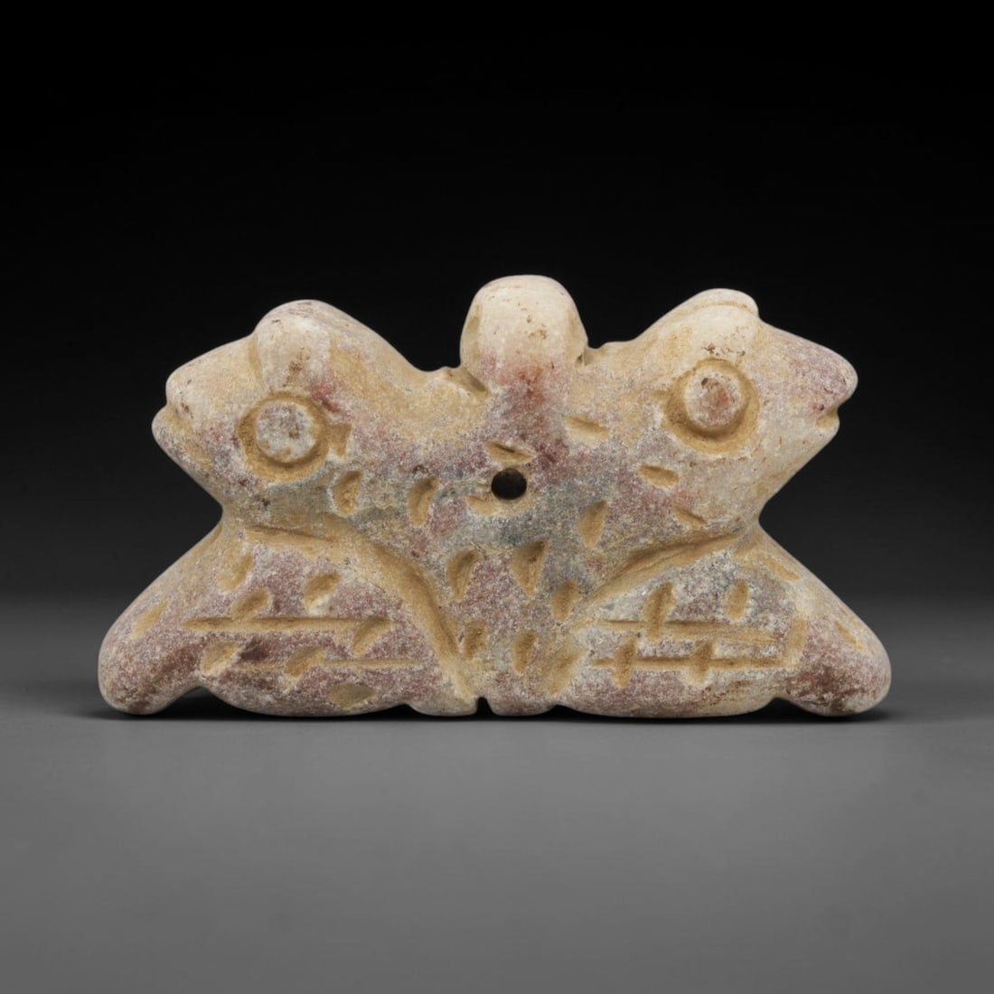 Ancient Stone Double Zoomorphic Amulet - Near Eastern, 27WJ: Carved from a fine-grained, pale stone with subtle reddish patination, this artifact takes the form of a symmetrical double zoomorphic amulet, depicting two confronting animal figures joined at a cent