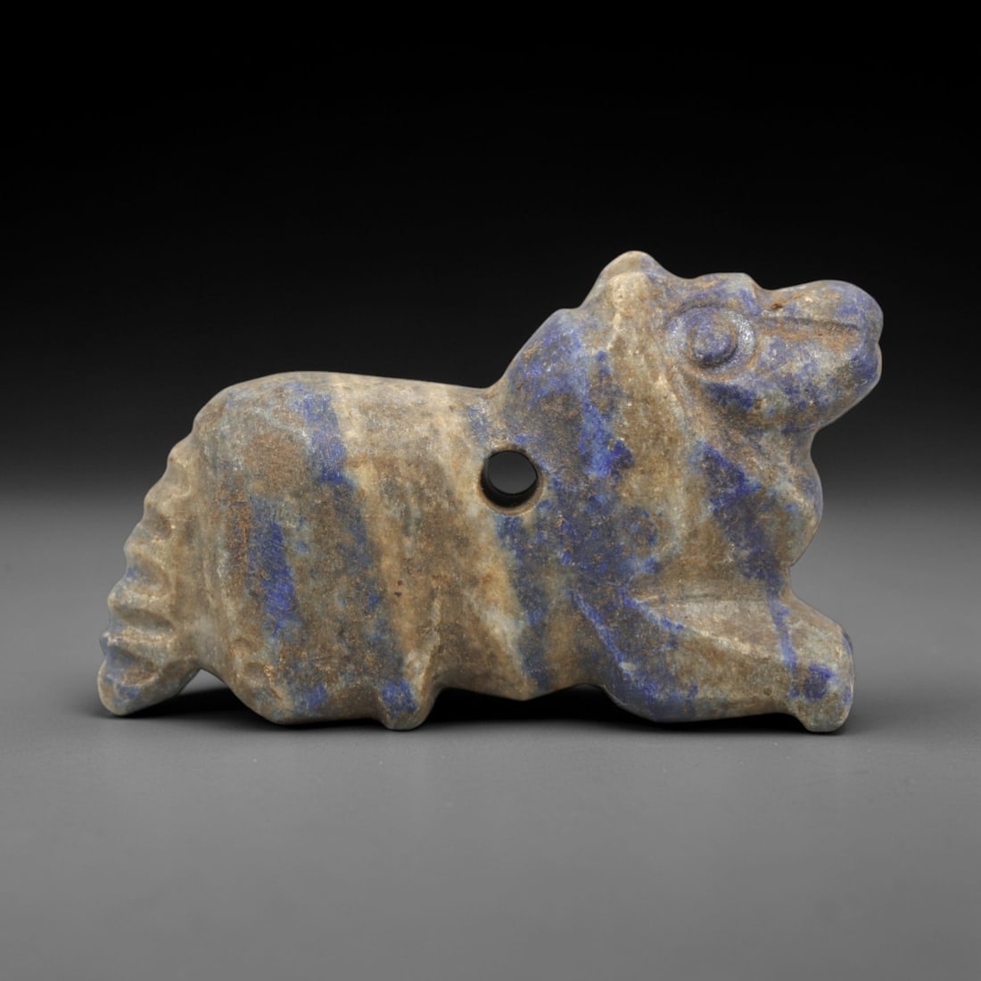 Ancient Lapis Lazuli Zoomorphic Amulet - Near Eastern Figurine, 25ZR: This artifact is a carved lapis lazuli zoomorphic amulet, executed in the stylized animal tradition of the ancient Near East. The amulet depicts a recumbent quadruped (likely a lion or canine) with si