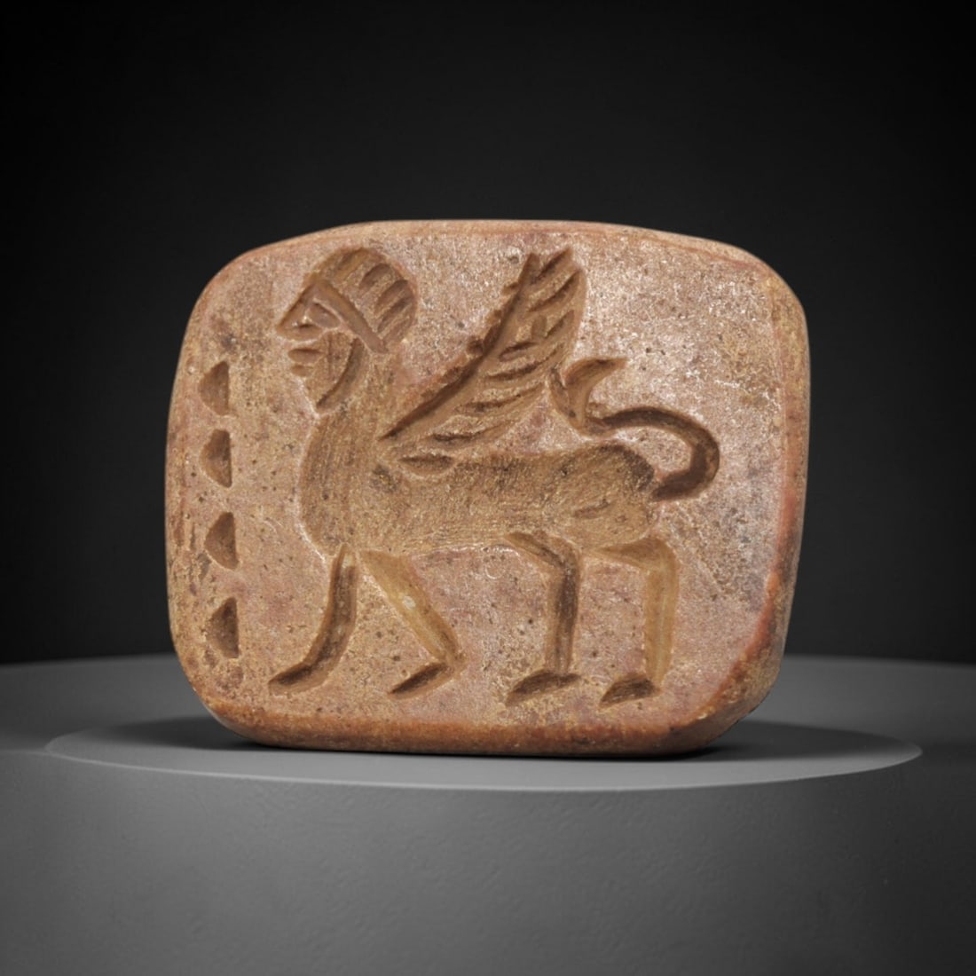 Ancient Steatite Stamp Seal - Near Eastern Sphinx Figurine, 98ZV: This ancient Near Eastern stamp seal is carved from steatite, formed as a rounded square plaque with incised decoration depicting a striding sphinx figure in profile, rendered with distinct linear det