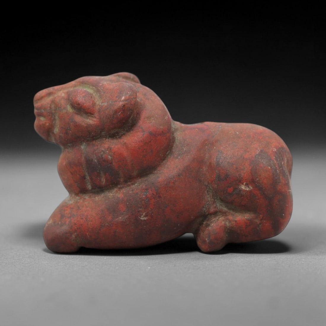 Ancient Near Eastern Red Stone Recumbent Ram Amulet - Carved Figurine, 9ZV: This amulet is carved from a rich, deep red stone with natural mineral speckling and patination, likely brecciated jasper or red steatite, featuring a stylized recumbent ram form. The piece displays a