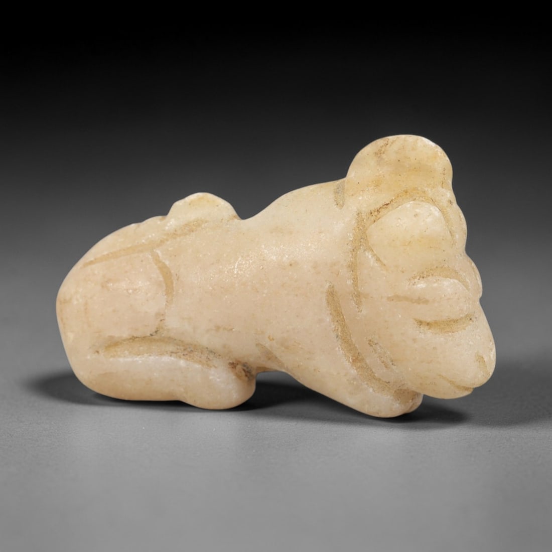Ancient Stone Feline - Near Eastern Animal Figurine, 72AR: This artifact is carved from a pale, creamy stone with a smooth, matte finish and subtle surface variations consistent with age. The form is a stylized feline, likely a lion or cat, depicted in a recu
