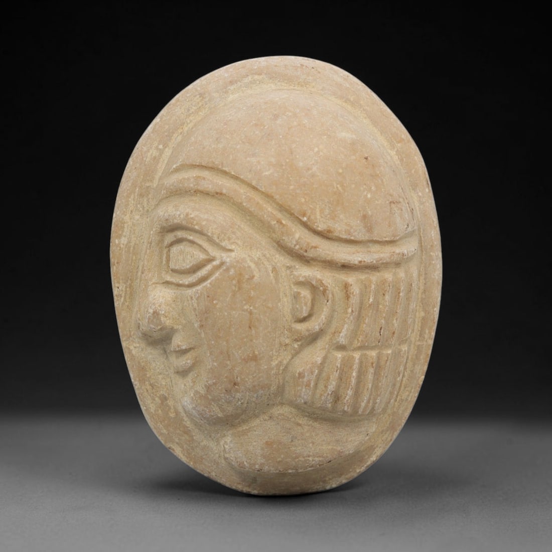 Ancient Stone Bust Amulet - Near Eastern Figurine, 91ZT: Carved from a fine-grained, pale limestone, this oval amulet features a raised relief depiction of a Near Eastern human bust in profile, with distinct stylized facial features, a structured headdress,