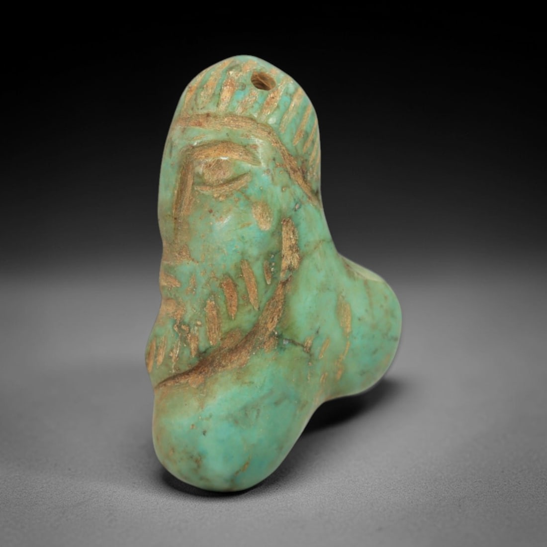 Ancient Turquoise Face Bead - Near Eastern Amulet, 83AK: Carved from polished turquoise, this bead-amulet depicts a stylized human face with incised linear details defining the eye, brow, and textured hair or headdress, with a suspension hole at the top for
