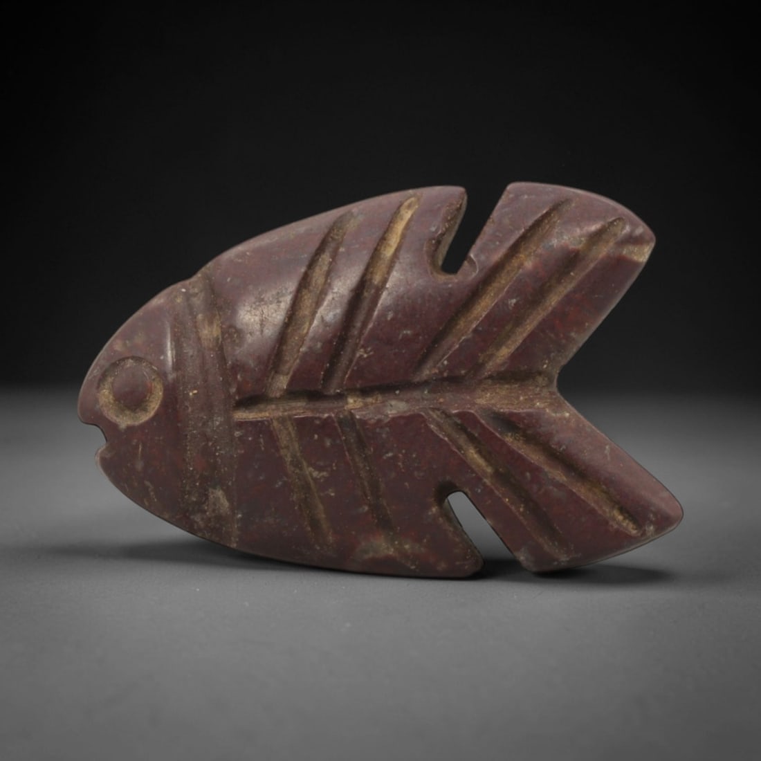 Ancient Stone Fish - Egyptian Amulet Figurine, 81XQ: Carved from deep reddish-brown stone, this amulet depicts a stylized fish with incised linear details defining its fins, tail, and facial features, including a circular eye and simplified mouth. The f