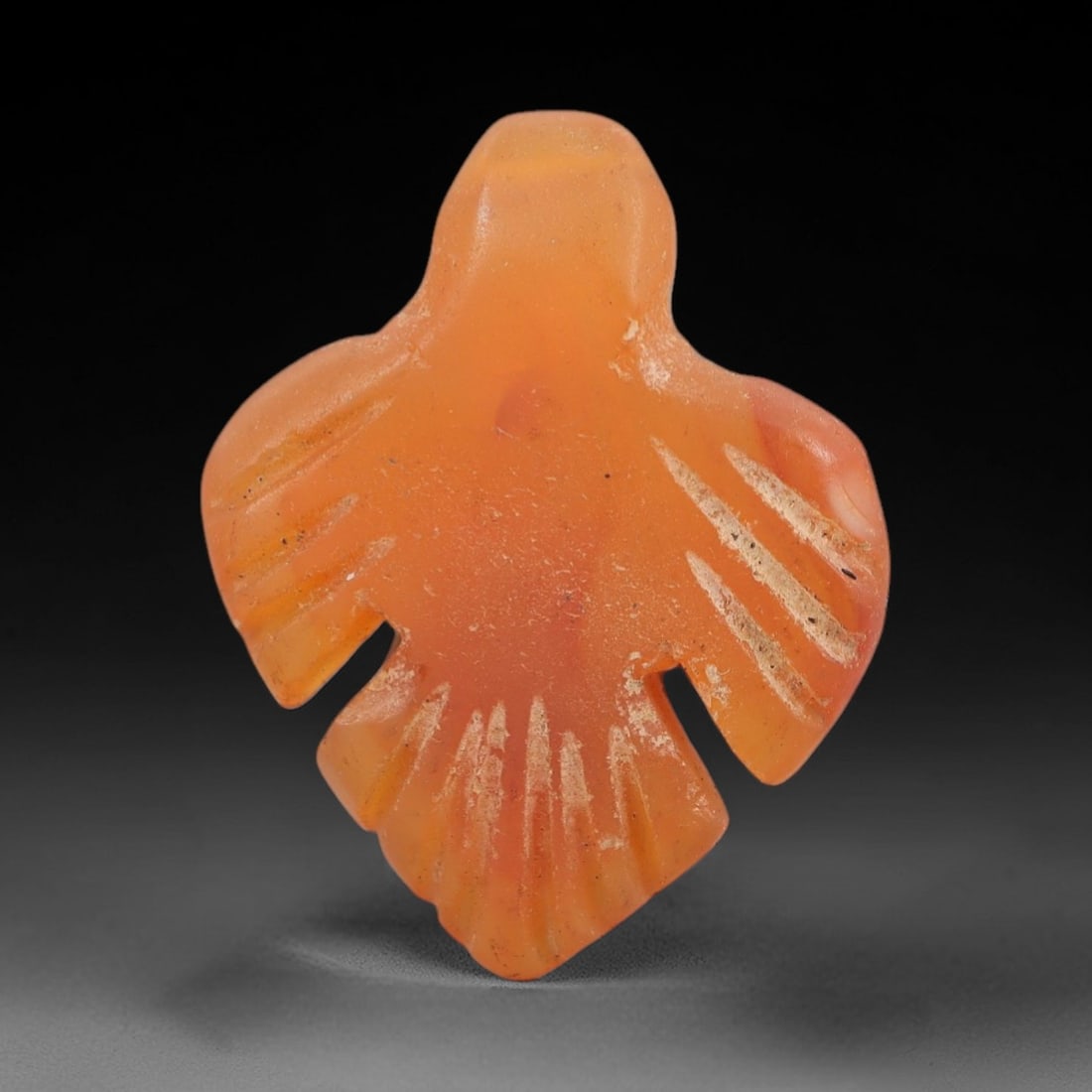 Ancient Carnelian Bird Amulet - Egyptian Figurine, 63AJ: Carved from warm orange carnelian, this amulet is formed as a stylized bird with fully outstretched wings and a fanned tail, featuring incised linear detailing across the wings and tail to denote feat