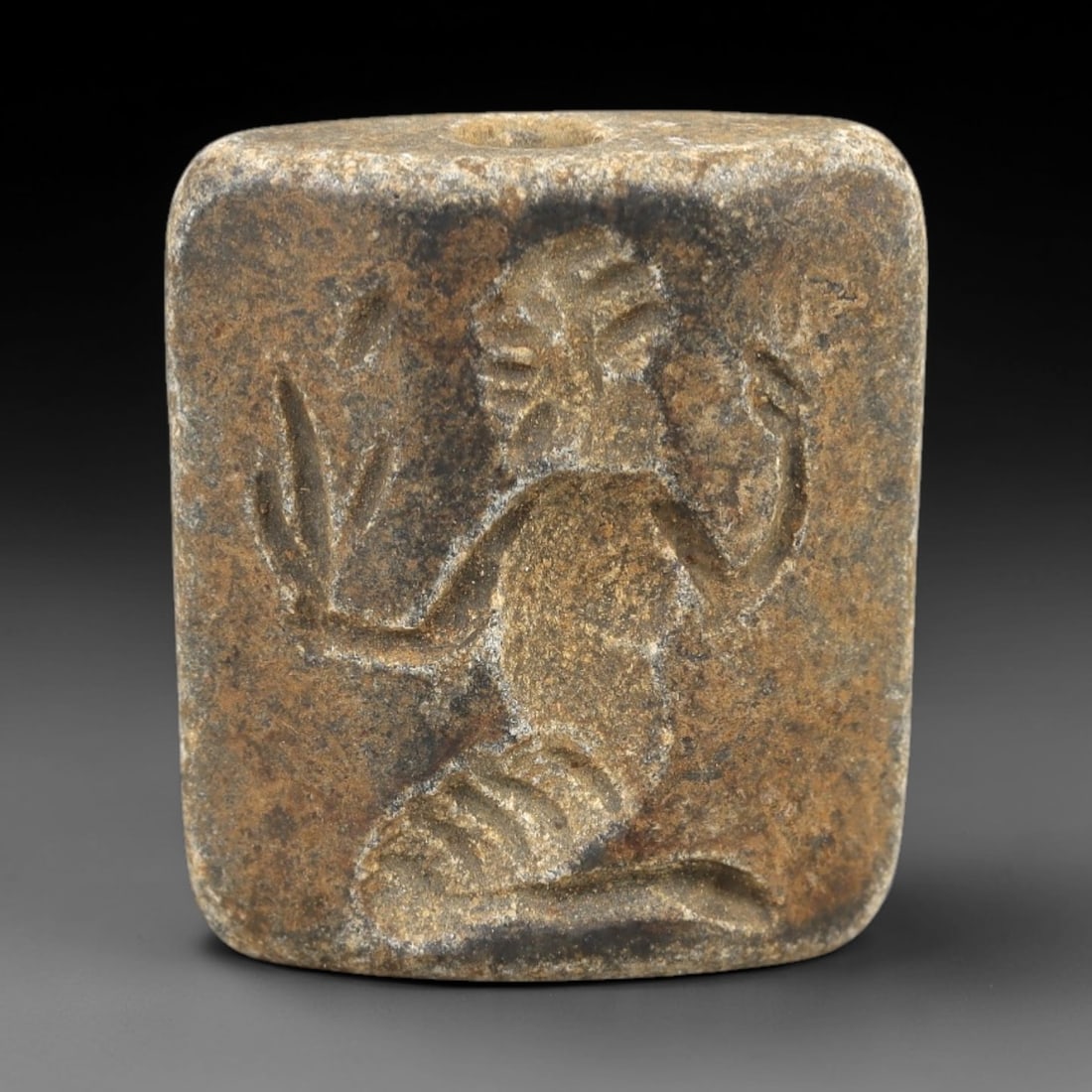 Ancient Schist Double Convex Bead Amulet - Near Eastern Deity Figure Intaglio, 77AM: Carved from dark gray schist, this 2.5x2cm double convex bead amulet features two distinct intaglio motifs: one side depicts a kneeling anthropomorphic deity with coiled lower body and raised hands, a